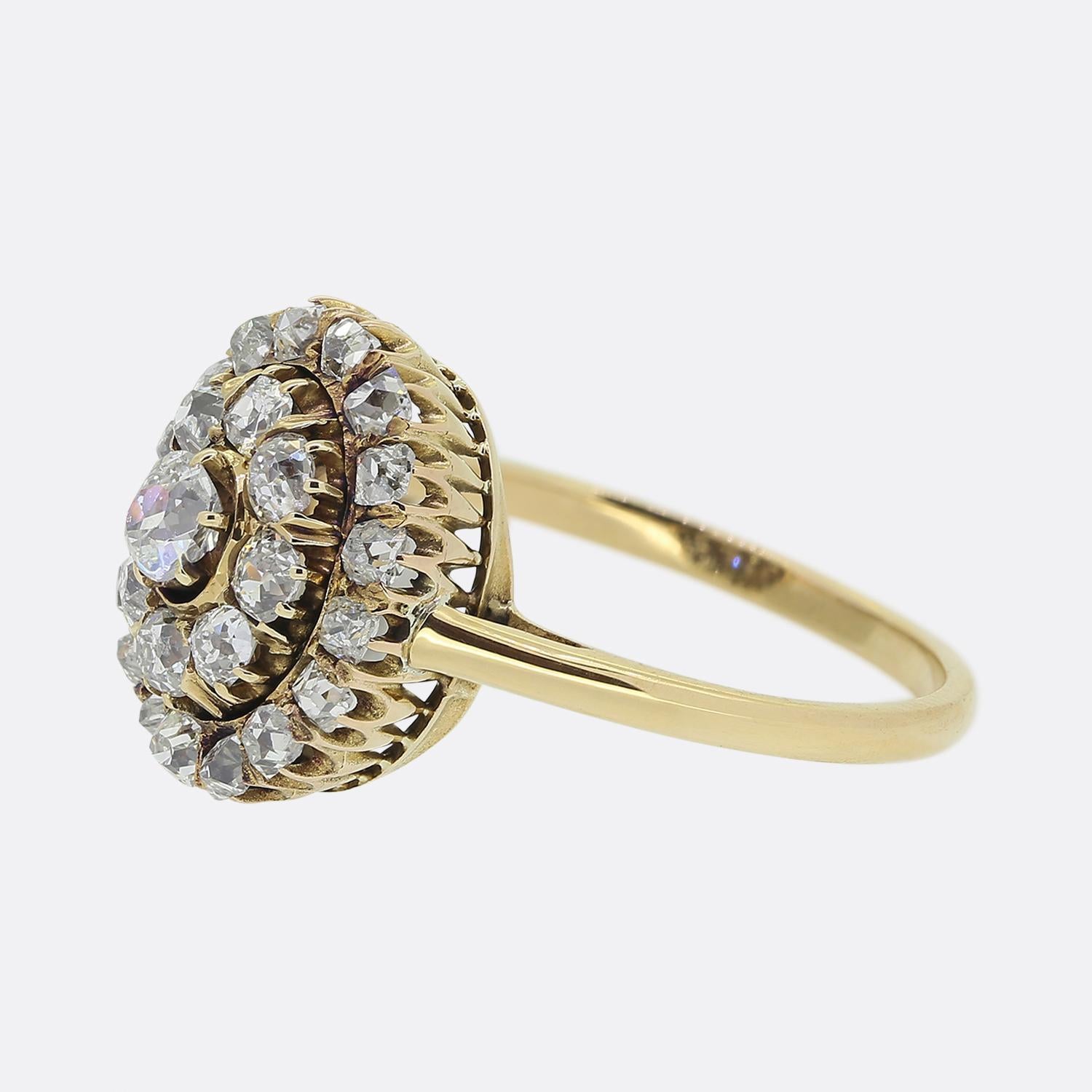 Here we have a charming diamond cluster ring from the Victorian era. This antique piece showcases an old cushion cut diamond at the centre of the face. This principal stone sits slightly risen and is surrounded by a double halo of chunky old cut