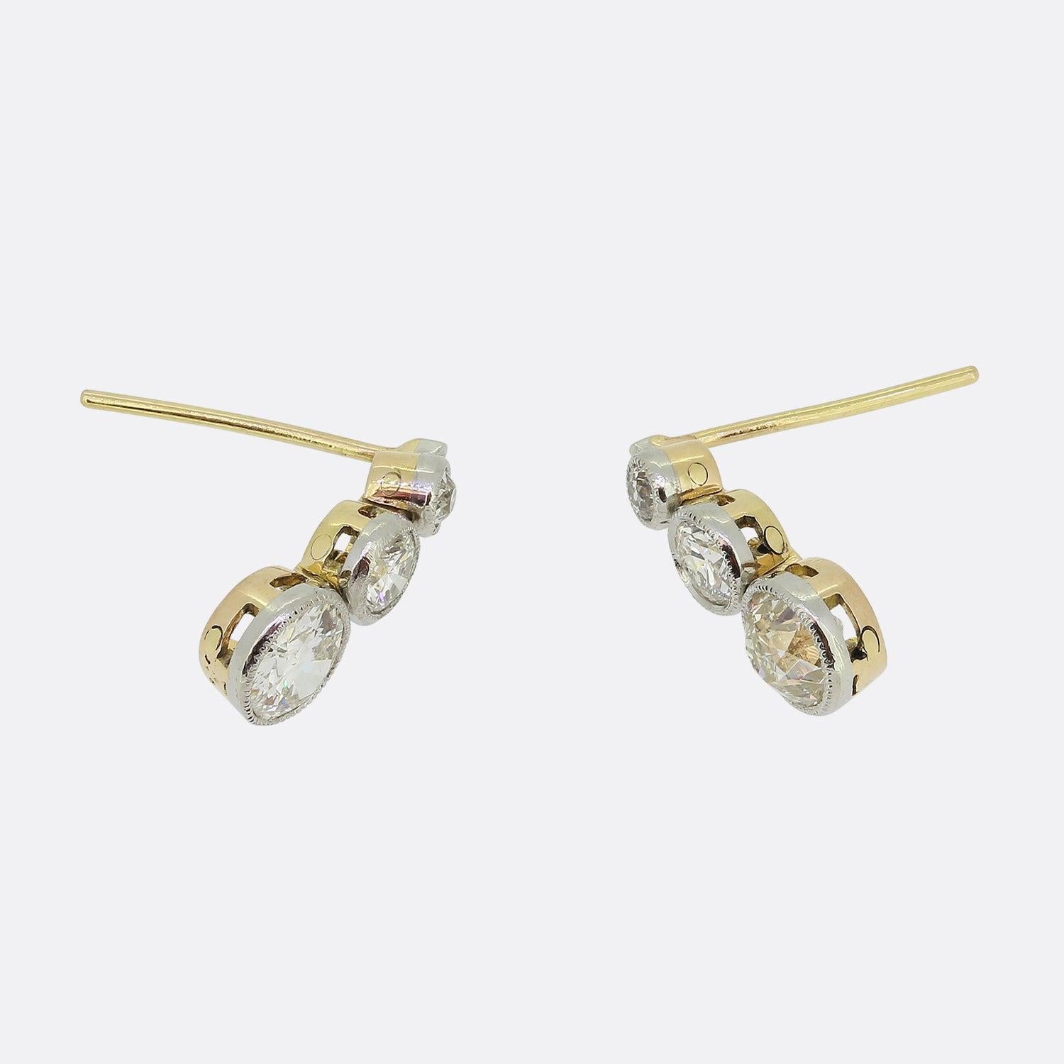 Here we have a wonderfully chic pair of 18ct yellow gold diamond drop earrings from the Edwardian era. Both pieces showcases a trio of round faceted old cut diamonds; each of which has been meticulously milgrain set in platinum and collectively