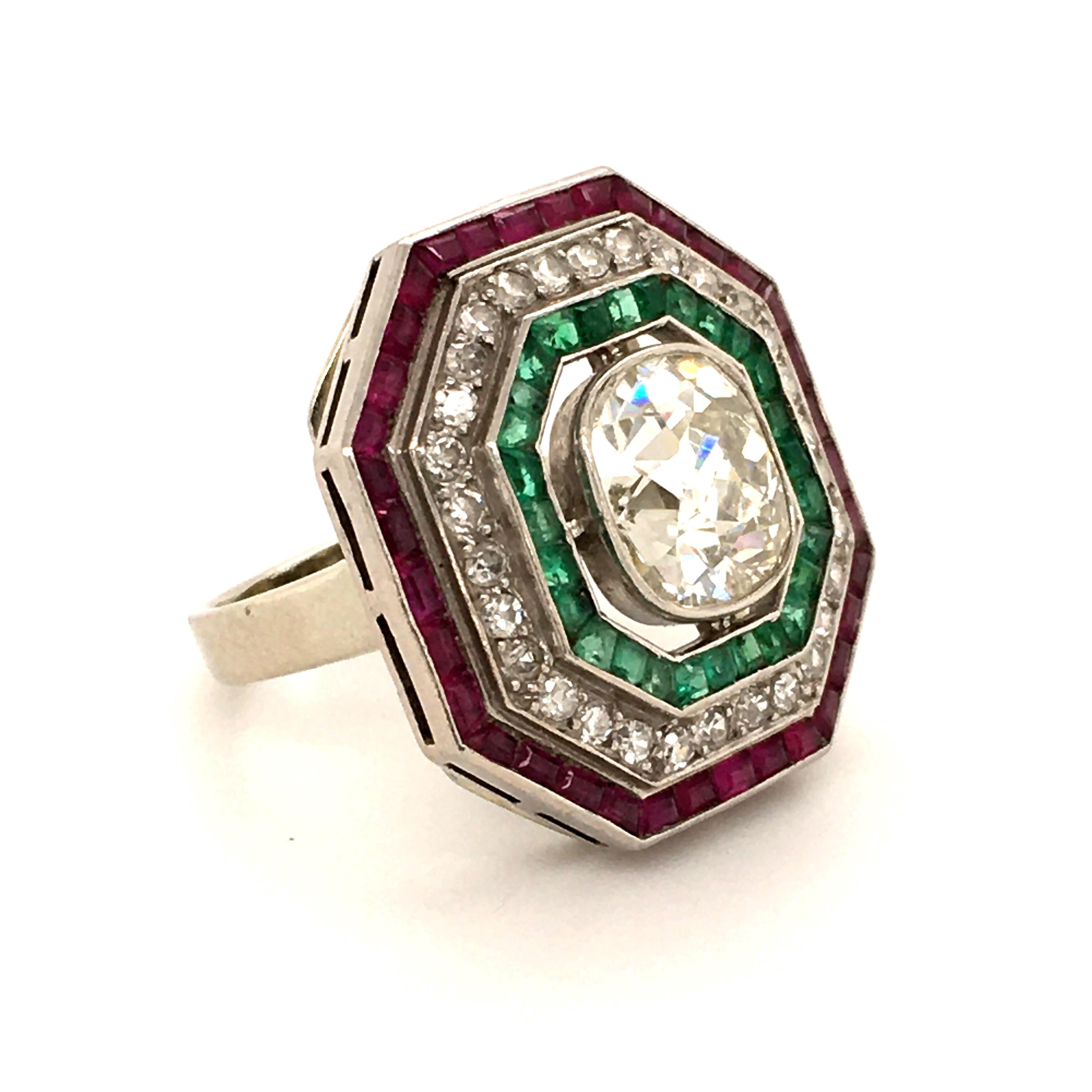 A fantastic tricolor antique diamond ring. The unusual octagonal outline certainly gives it an Art Deco look. Three rows individually channel set with rubies, diamonds and emeralds. Finished in the center with a beautiful old cushion shaped diamond