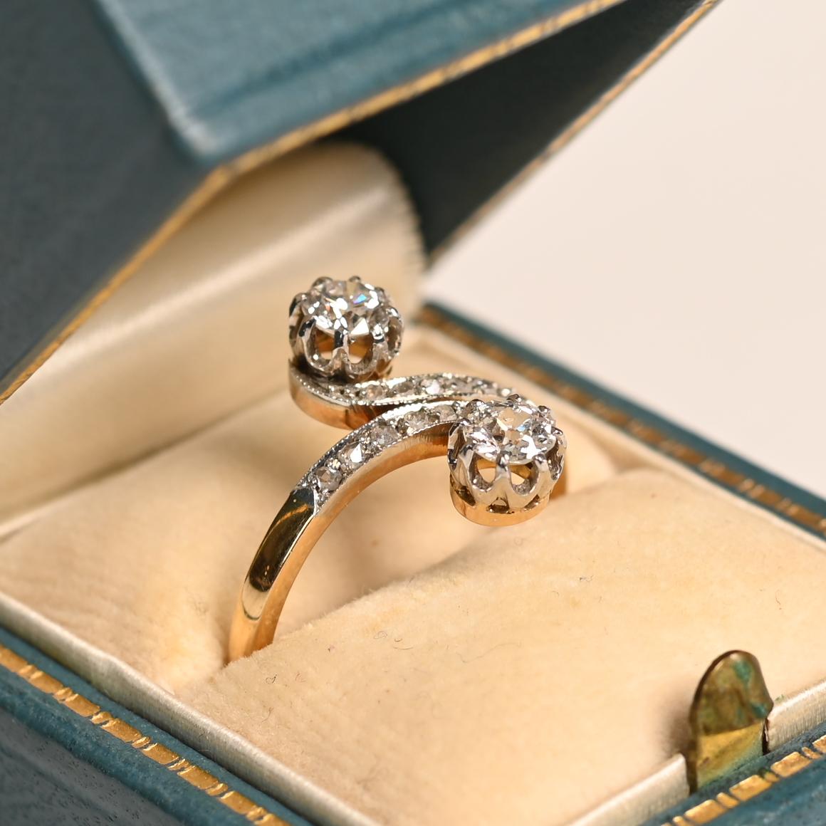 Questo squisito anello antico in stile Art Nouveau, realizzato a mano in Francia intorno al 1900, mostra un'armoniosa miscela di eleganza e maestria. Al centro, due diamanti abbaglianti - un distinto taglio europeo antico e un luminoso taglio