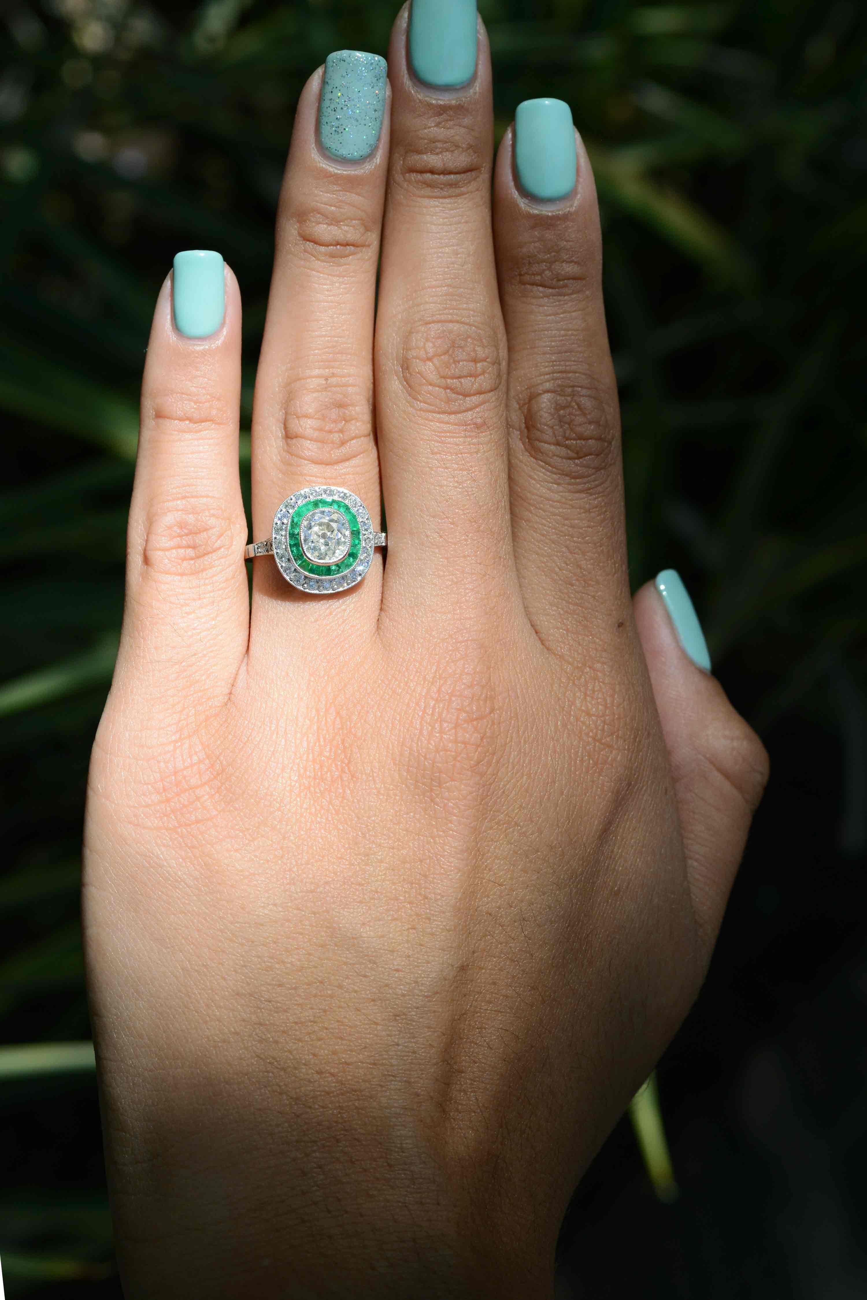 A magnificent antique old mine cushion cut diamond & emerald engagement ring headlining an exquisite double halo. The partition of perfectly matched French cut emeralds glow incredibly and are a standout element in this stunning piece. The center