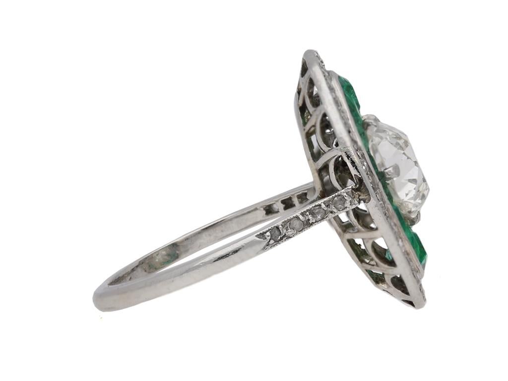 Old mine diamond and emerald ring. Set with one central cushion shape old mine diamond in an open back claw setting with a weight of 2.01 carats, set into a vertical oval bezel set with fourteen tapered baguette cut natural emeralds with no colour