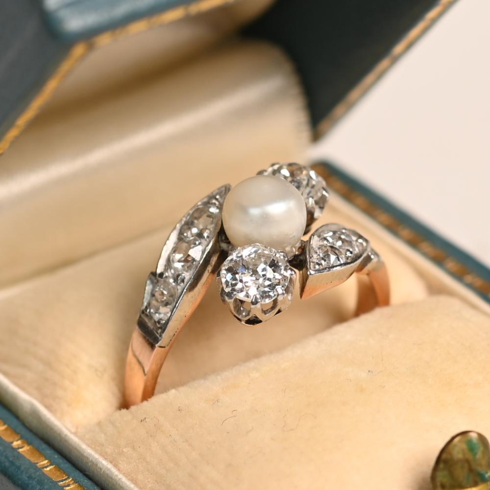 Dieser exquisite antike Verlobungsring mit drei Steinen präsentiert eine leuchtende Perle, die von zwei Diamanten im alten Minenschliff in einer anmutigen diagonalen Anordnung flankiert wird. Die Diamanten, die sicher in Zackenfassungen gehalten