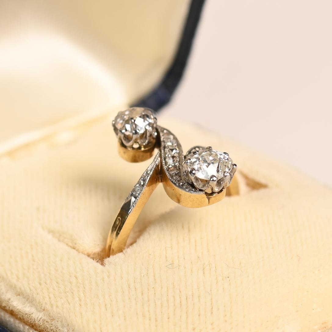 Este exquisito anillo francés antiguo, fabricado en la época eduardiana hacia 1900, exhibe dos cautivadores diamantes talla mina antigua con un peso combinado de aproximadamente 0,8 quilates. Estos luminosos diamantes, de color I y claridad VS2-SI2,