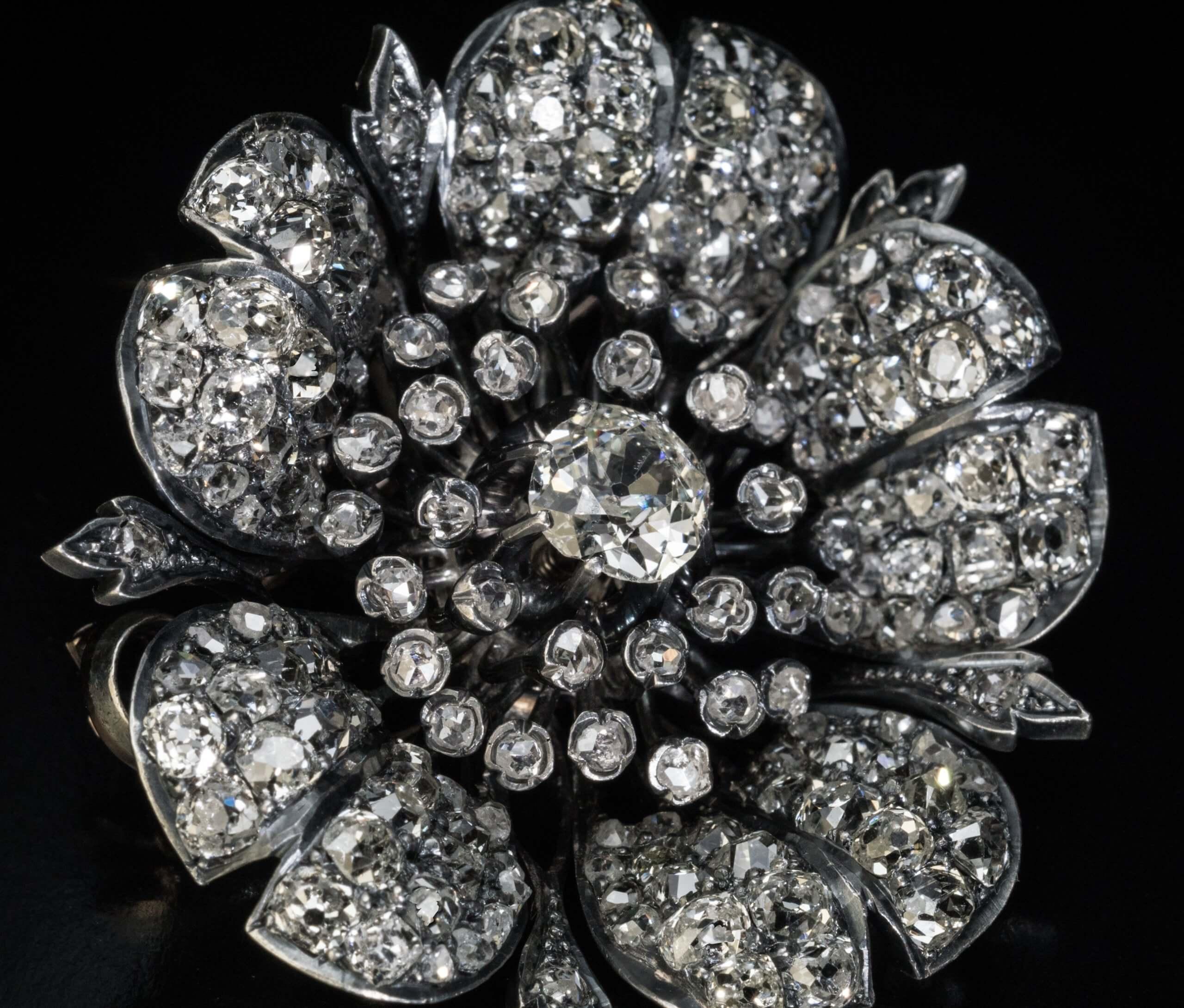 Circa 1880s – 1890s  This Victorian era flower head brooch is finely crafted in silver topped 18K gold (front – silver, back – gold). It is centered with an old mine cut diamond (6.4 x 6.3 mm, approximately 1.10 carats) surrounded by numerous rose