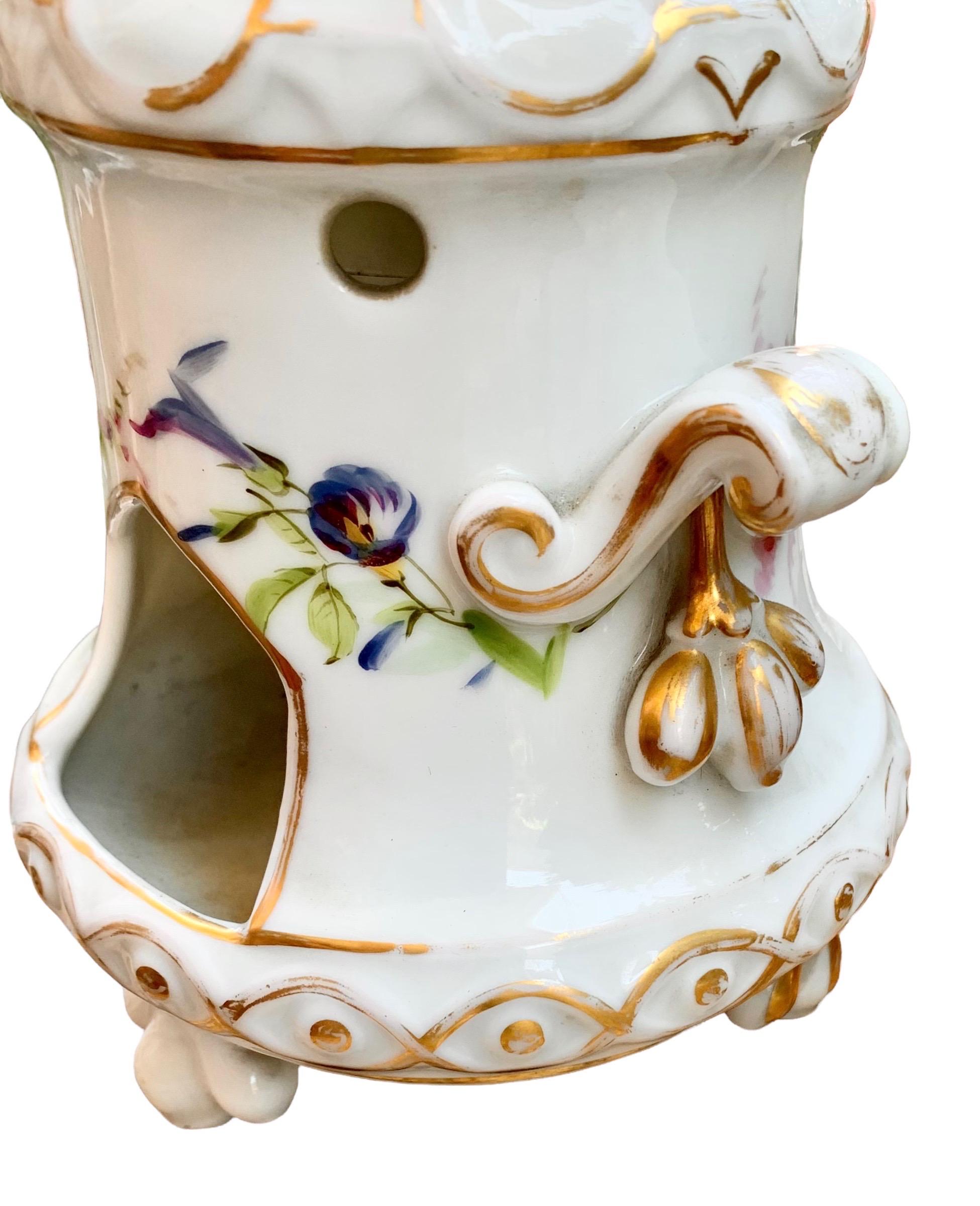 A fine 19th century Hand-painted and gilt decorated porcelain veilleuse, depicting floral studies. It rests on three tripodal feet and has lovely scroll handles and clusters of fruit.

In the warming stand one would have placed a candle or oil to