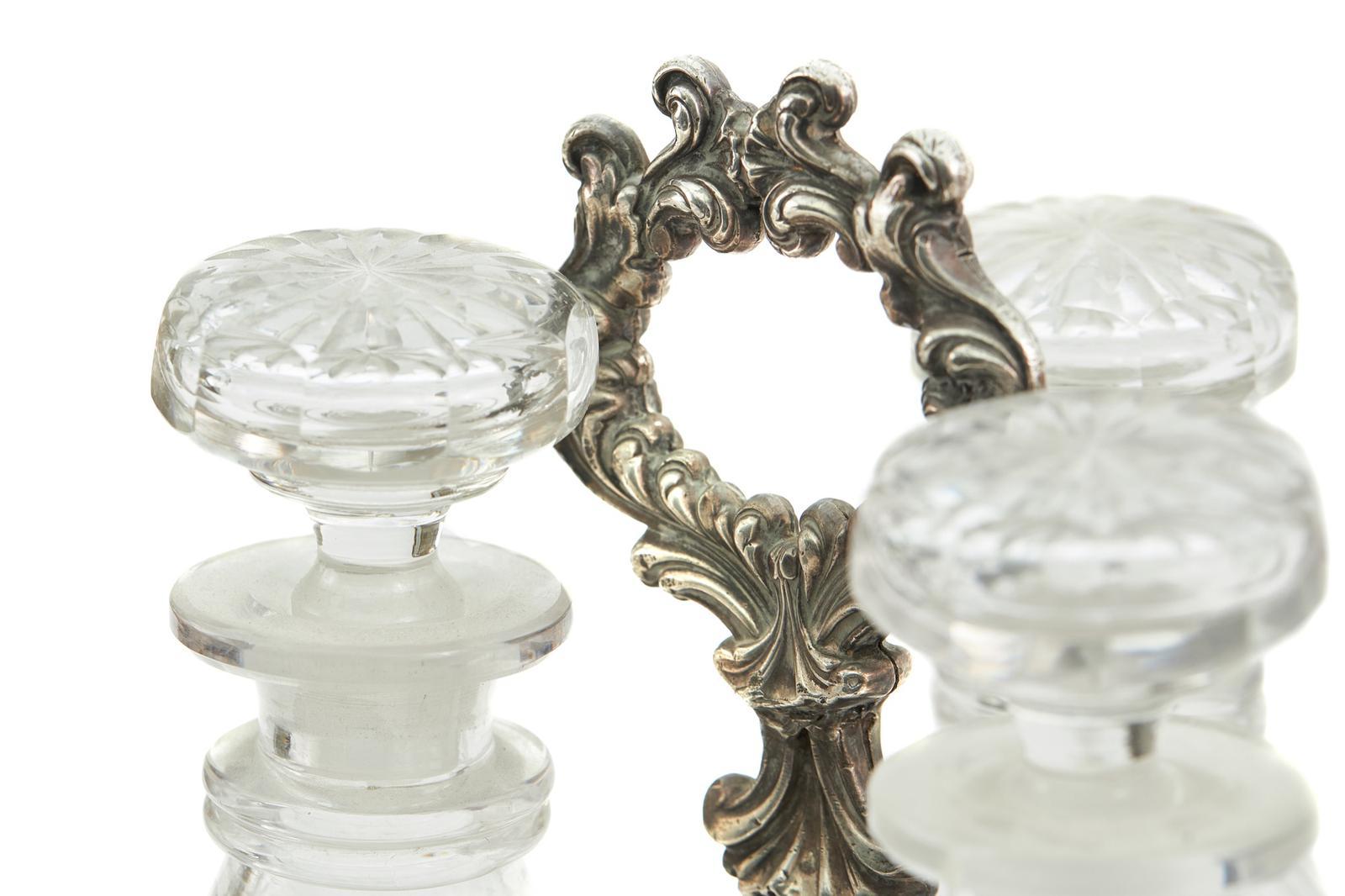 Ancienne cruche à décanter à trois bouteilles en tôle de Sheffield, avec une poignée à boucle et une bordure à volutes, reposant sur des pieds à volutes percés, avec trois carafes en verre taillé et les bouchons d'origine.