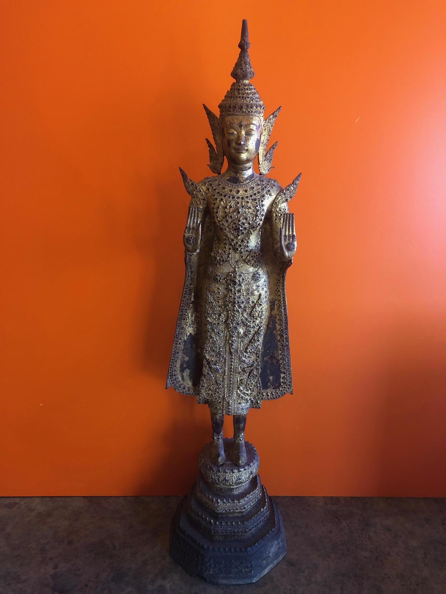 Antique Old Siam / Thai lacquered gilt bronze Ayuttaya Buddha, circa late 1800s. The piece is heavily gilded and richly ornamented with armbands, bracelets and anklets. The Buddha’s austere countenance seems to smolder and glow, highlighting the