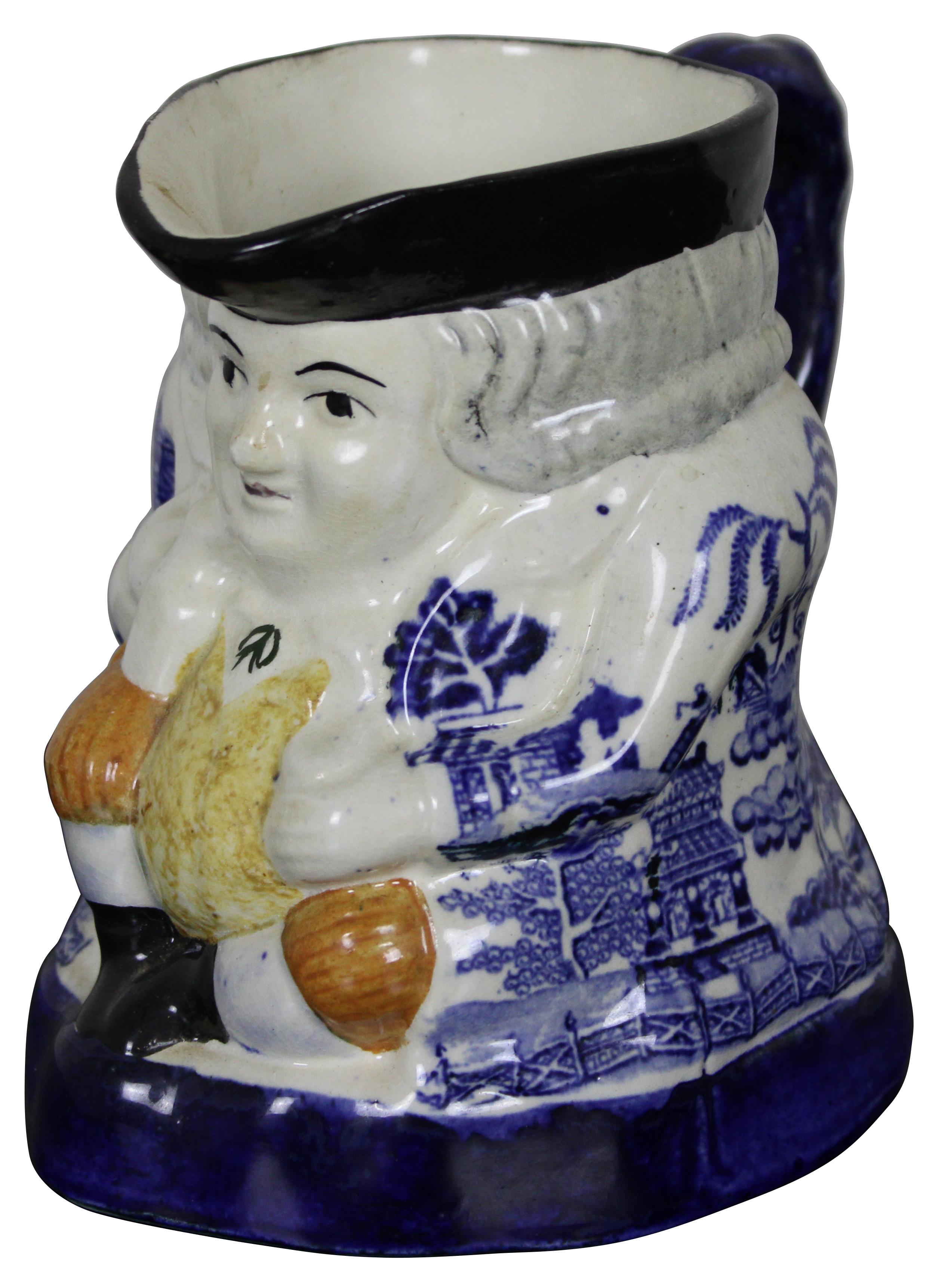 Antique turn of the century Old Staffordshire rare pottery toby jug in the shape of a colonial Englishman holding a cup and pitcher, and decorated with a chinoiserie blue willow pattern around the sides. Measure: 6