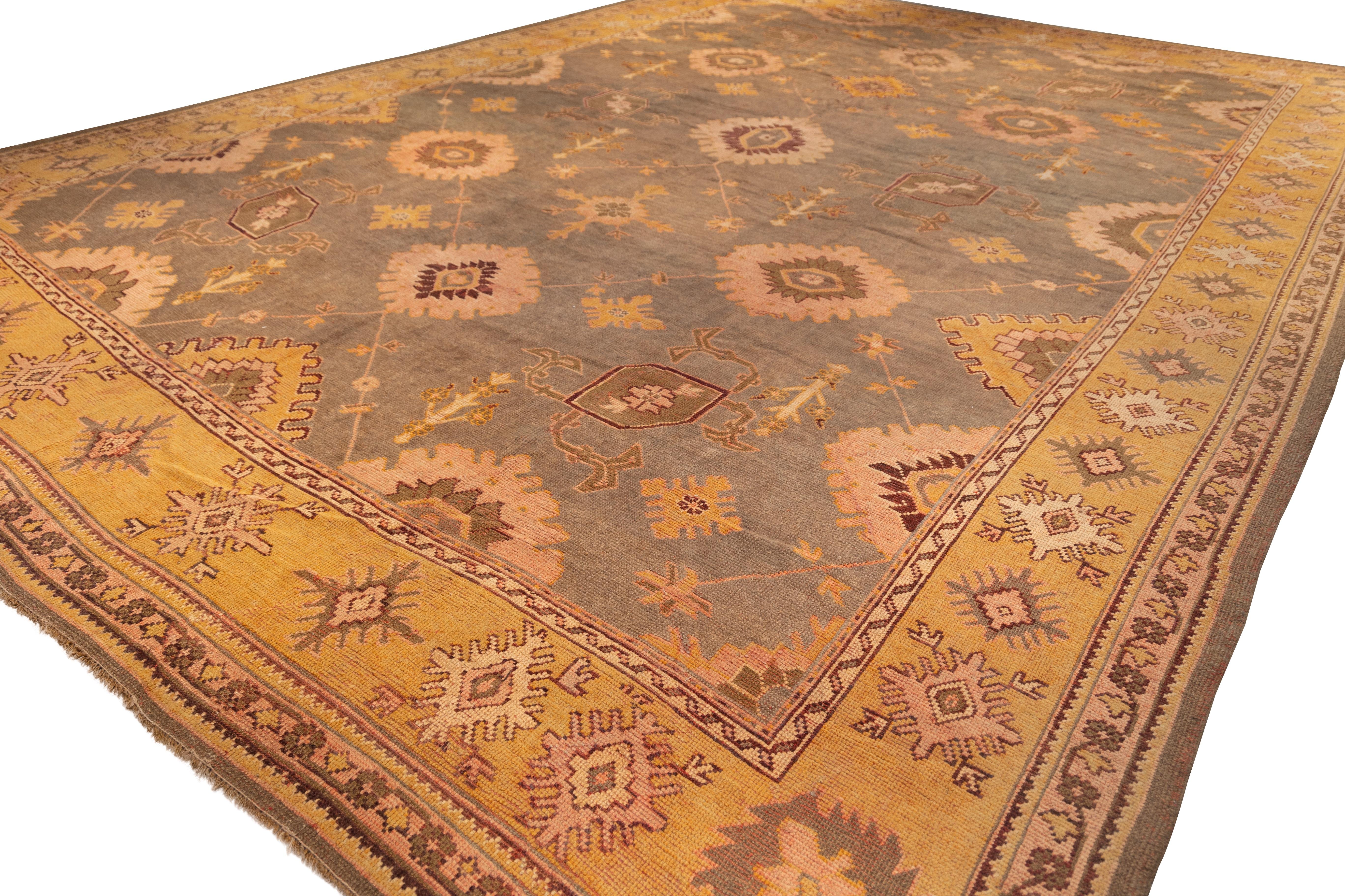 Oushak rug features a soft Olive-brown field with a scattered pattern of large medallions, floral rosettes, and geometric motifs in light peach, gold, and muted burgundy. The border in warm yellow carries a repeating star-like design, tying the
