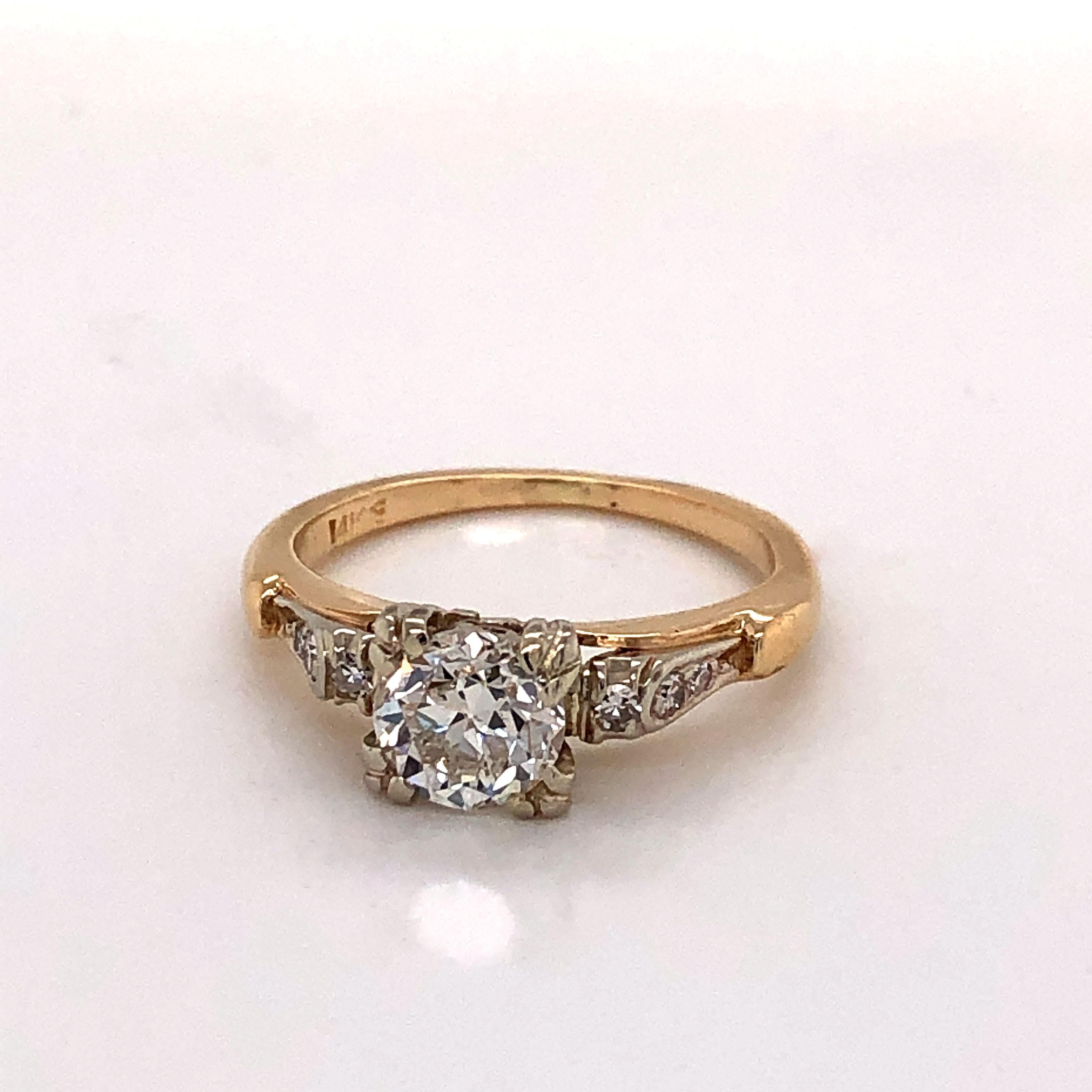 This elegant antique ring in fourteen carat yellow gold (14k) features a one carat (1 ct.) J/VS prong set round Miner's cut diamond flanked by baguettes of three smaller bezel set diamond accents on each side that graduate back along the band. Ring