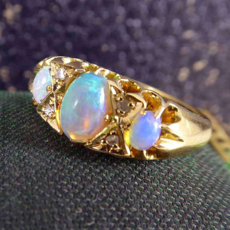 A very pretty opal and diamond set ring centring on an oval, cabochon-cut opal to the centre.  On each side of the principal opal , in a bow-shaped setting are two rose cut diamonds before the gem stone arrrangement terminates in a small, oval,