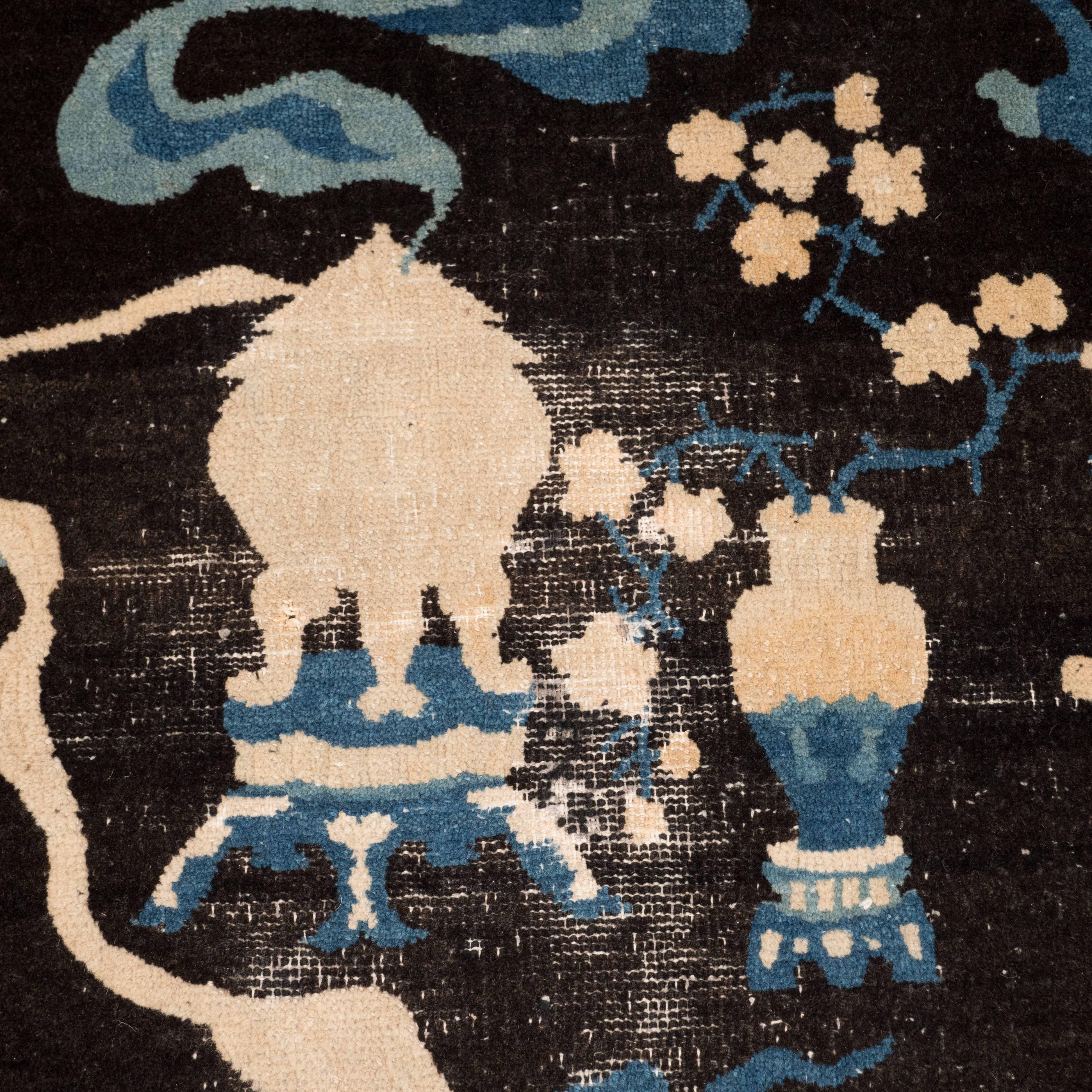 This graphic and sophisticated Ming rug was realized in China, circa 1880. Presented against a black background, the circular rug presents sprigs of cherry blossoms resting in a vase, as well as a pagoda style incense holder with claw style feet