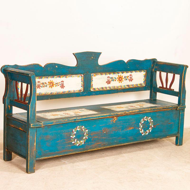 This delightful storage bench from Hungary still maintains its original blue paint. The charming flowers and wreathes on the front were a traditional folk art style of the period. The hinged seat with the paint slightly worn from years of use, lifts