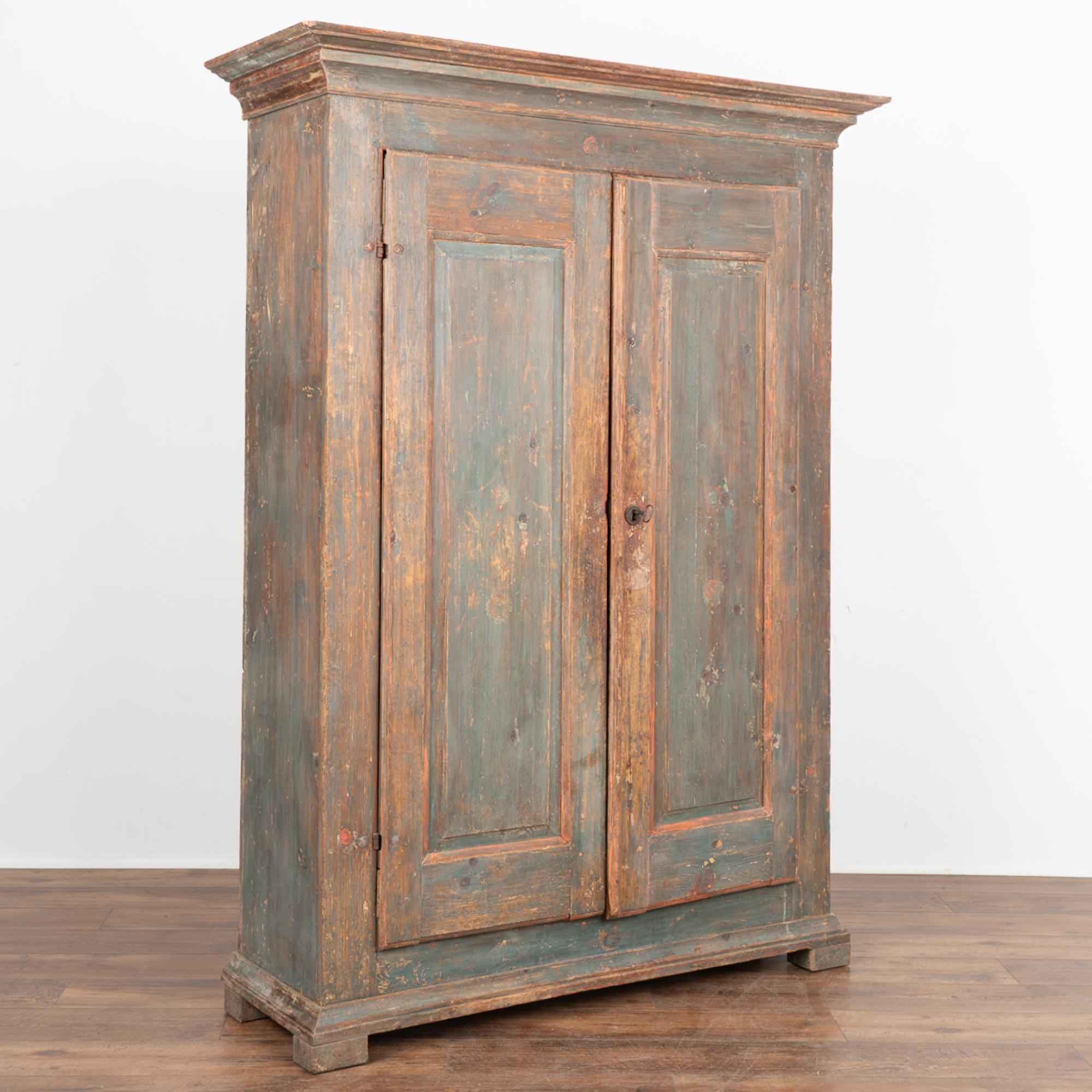 It is the incredible aged patina of the original painted finish that makes this armoire a special find. Look closely and you will see the residual image of red flowers against the faded blue background.
The interior still has the carved wooden pegs
