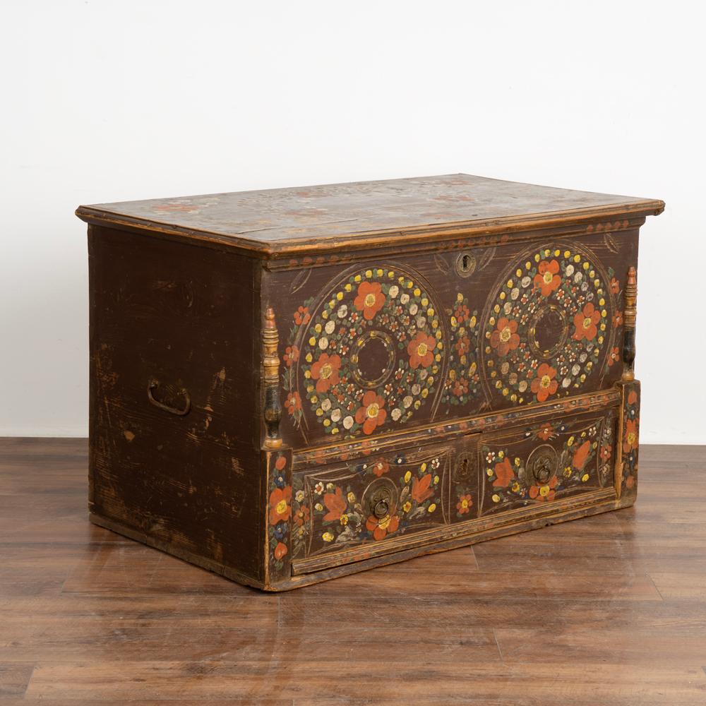 Antique original hand painted folk art flowers in orange, green and yellow are still prevalent on this large trunk.
Half column accents, wrought iron handles, and lower functioning drawer.
Front panel carving and traditional interior 