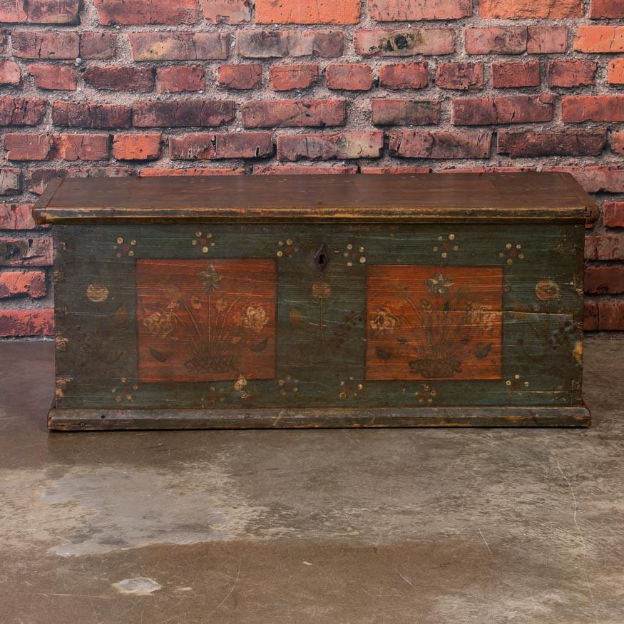 Aside from the charming original paint, it is the areas that have been gently worn away from years of use that attract one to the country appeal of this flat top trunk. The rich, rust colored panels surrounded by a blue green background are worn in