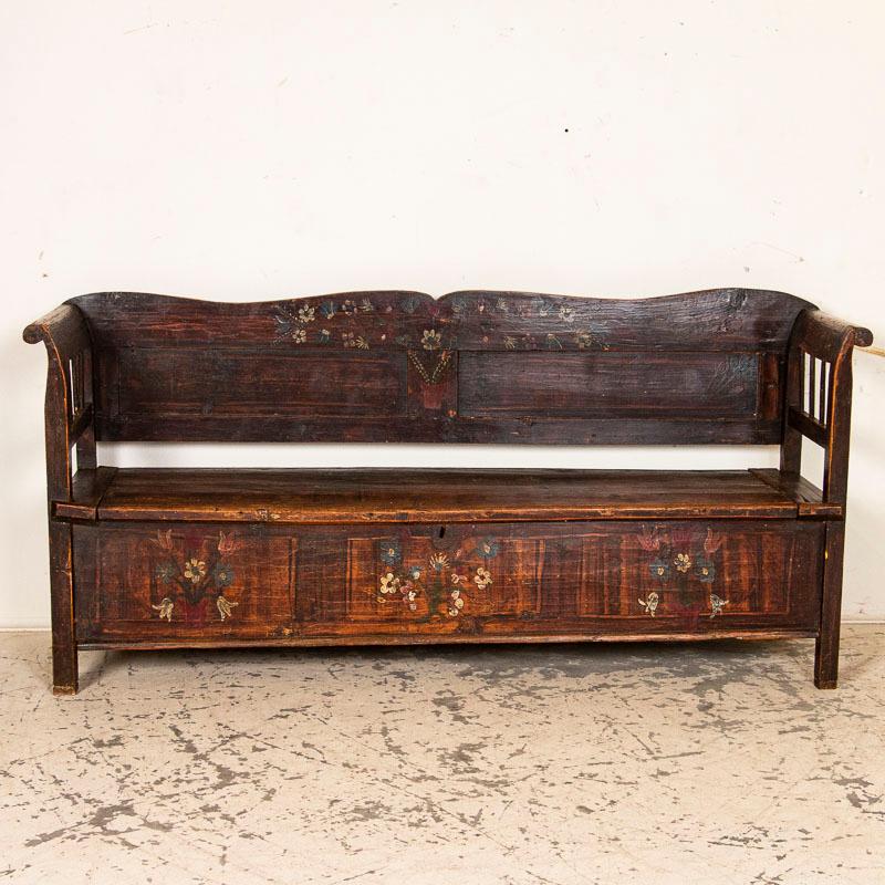 This bench has a romantic country feel to it thanks to the original hand painted details that still remain and the gently curved back and arms. The brown painted faux wood finish (traditional for the era) is highlighted with traditional floral