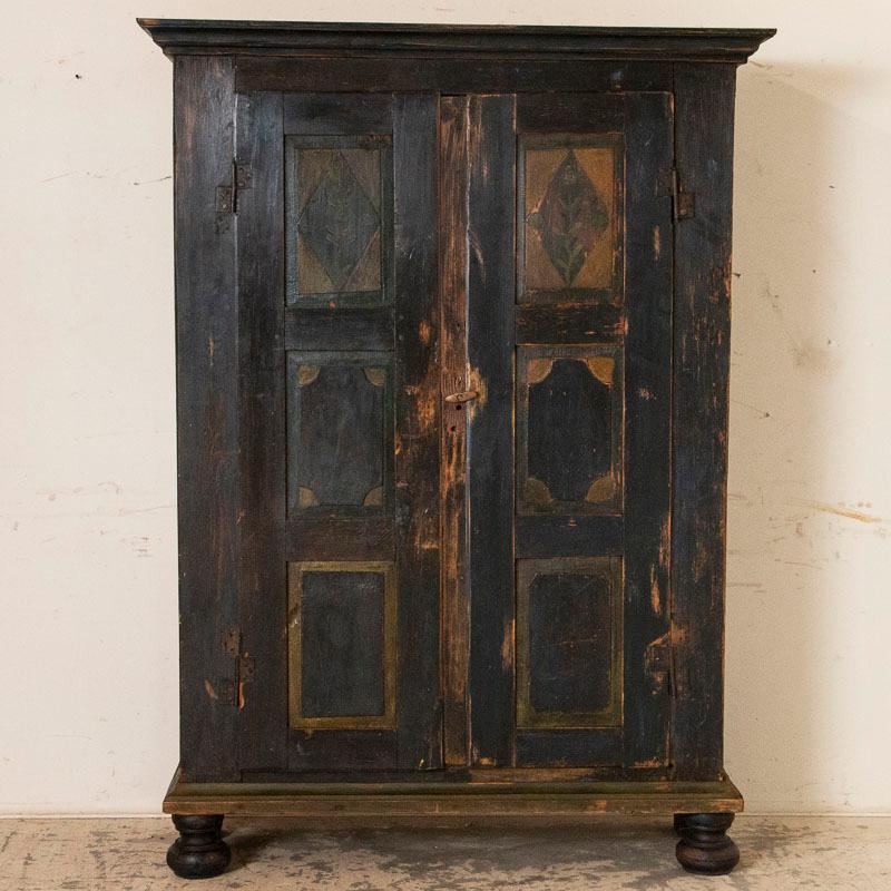 While visually this armoire appears black, it is actually a very dark navy blue that accents this endearing primitive armoire from Lithuania. The heavy pine armoire shows its age in every age-related crack and gouge. It is distressed especially