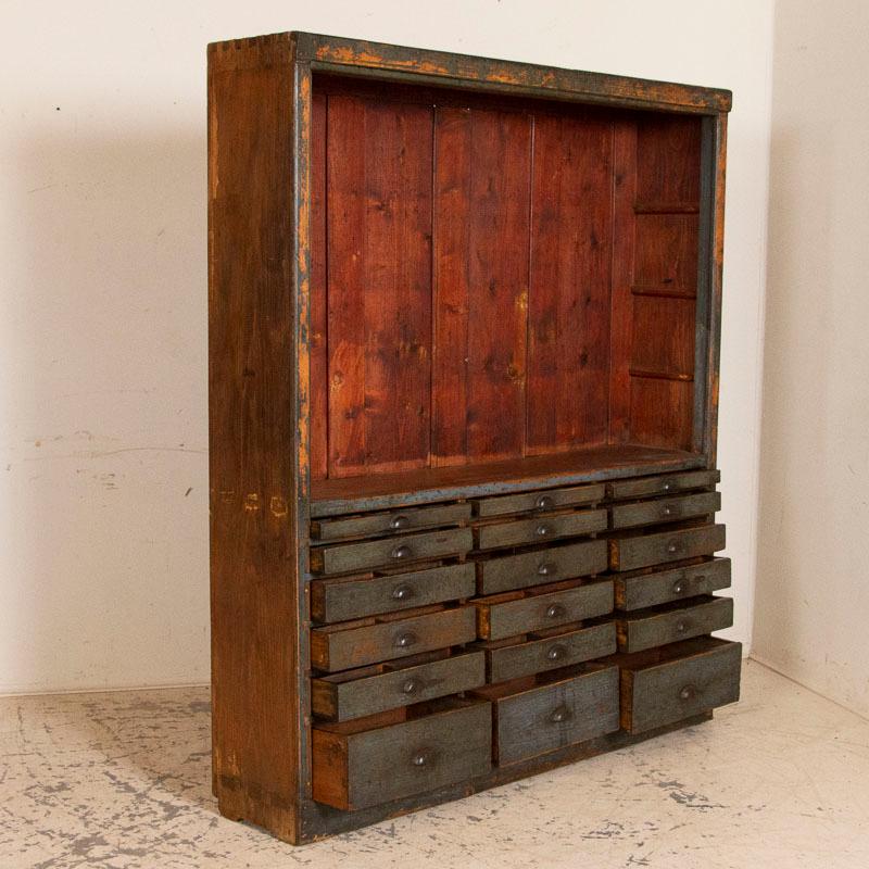 This vintage cabinet originally started life as a shop display wall unit. It is the distinctive slate blue/gray color (with hints of green as well) that captures one's attention. The original paint has been worn off through years of use to reveal
