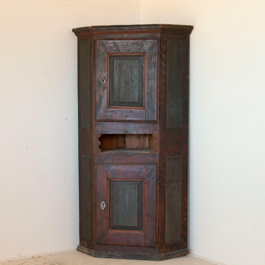 This charming hand painted Swedish corner cupboard still maintains its original paint, with deep dark green panels and a traditional background in earth-toned colors with reddish base. The traditional Folk Art style of the period was to paint a faux
