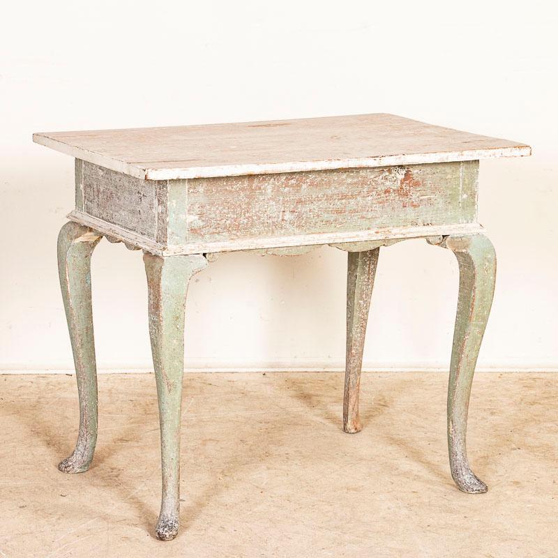 It is the original seafoam and white painted finish and gently curved cabriolet legs that attract attention in this endearing Swedish gustavian side table. The paint had been gently distressed through generations of use which instills an aged grace
