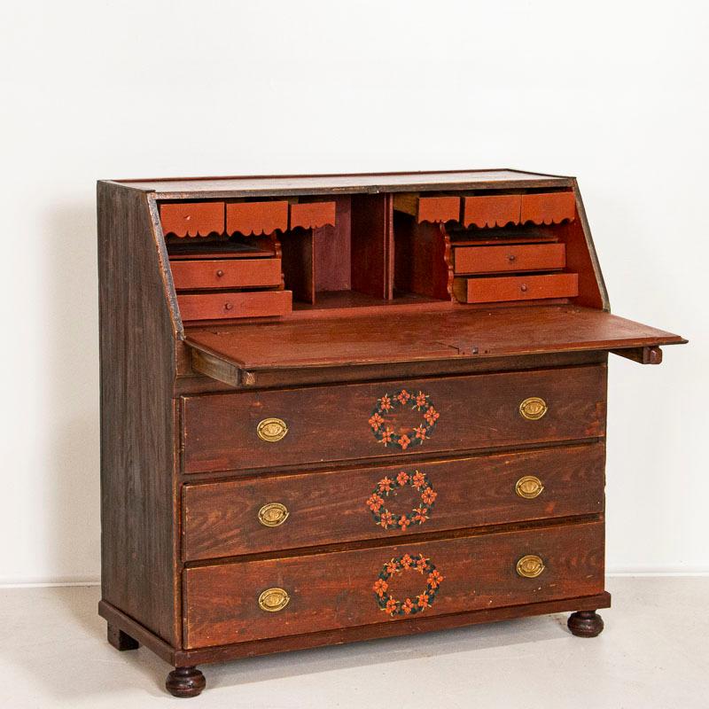 The red hue painted finish is all original in this Swedish secretary, also known as a bureau. The hand painted flower garlands add a joyful touch to the drawers and desk top exterior. Two wood 
