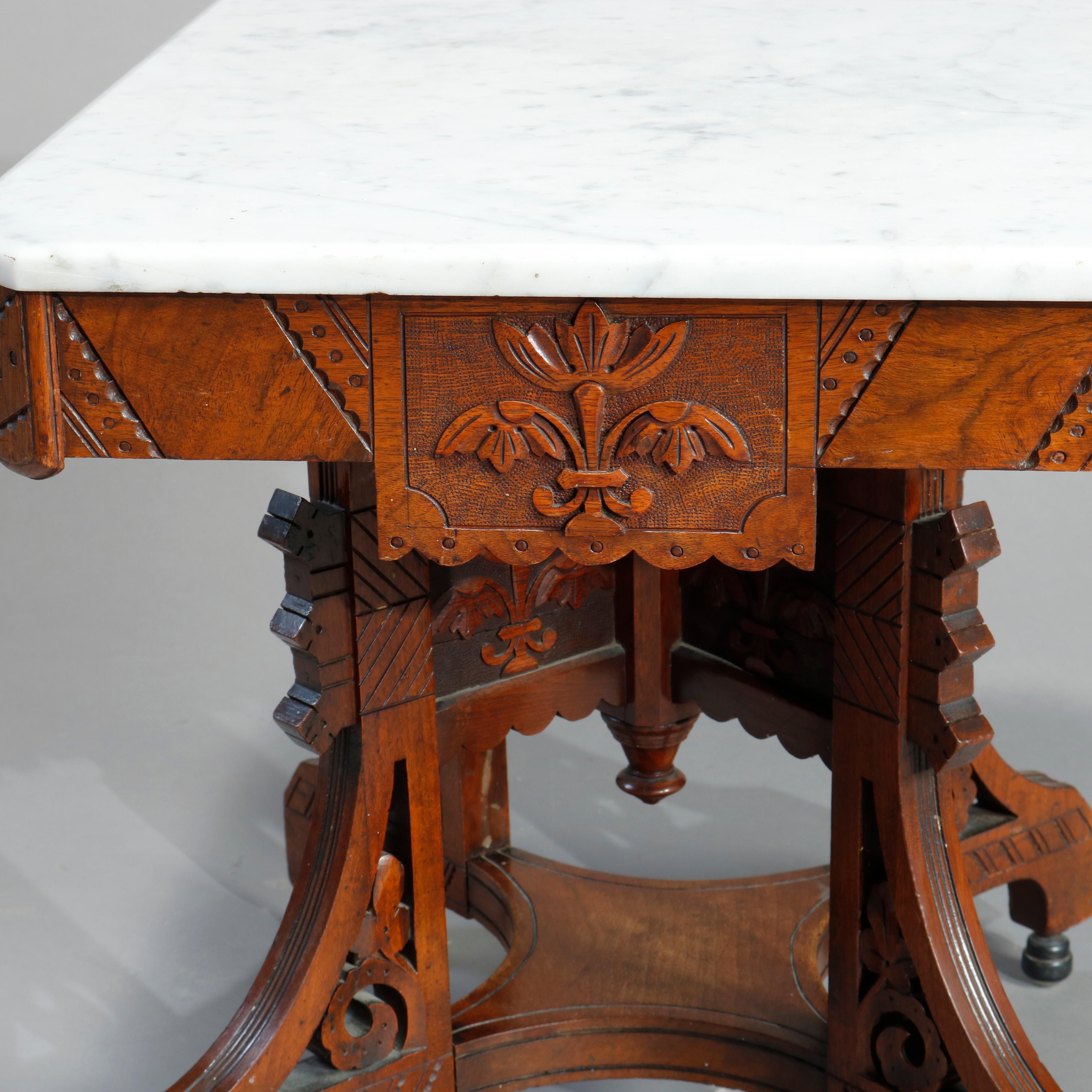 An antique and ornate Eastlake coffee table offers clip-corner marble top surmounting carved rectilinear walnut base having carved stylized floral elements in relief and incised linear decoration, legs with scrolled elements, central drop finial and