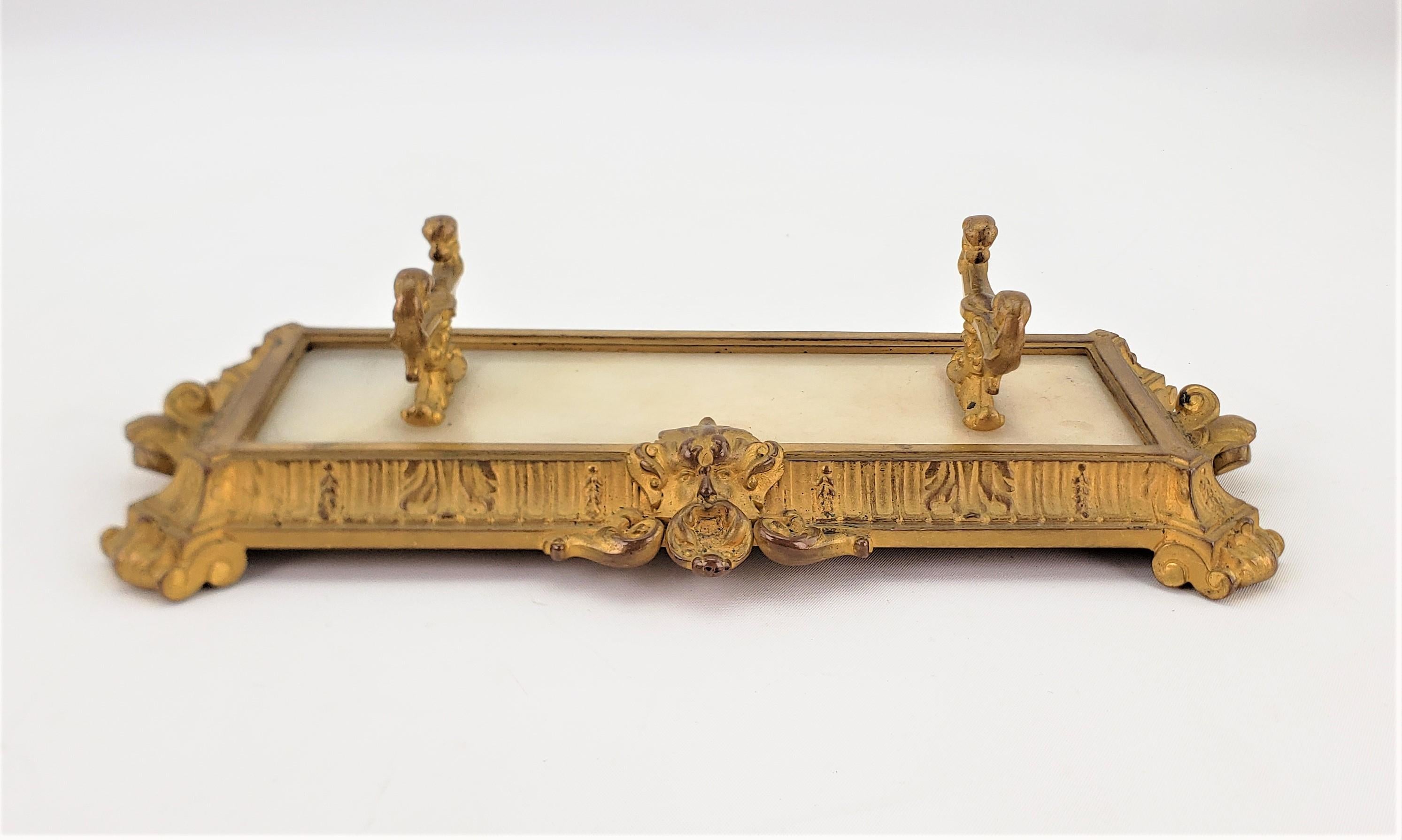 This antique pen rest or holder is unsigned, but presumed to have been made in the United States in approximately 1900 in the period Edwardian style. The frame and pillars of the pen rest are made of cast bronze with a gilt patination and has