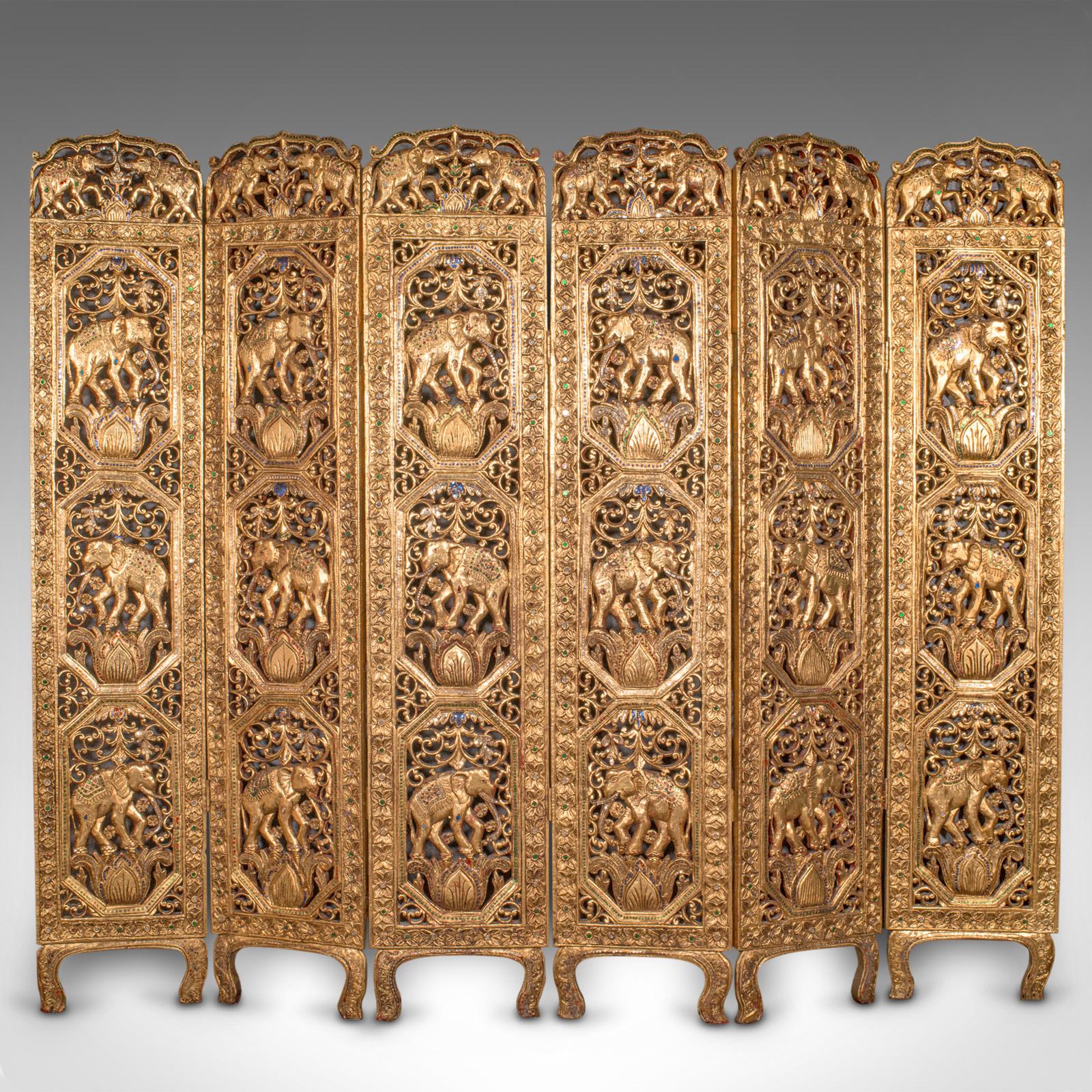 This is an antique ornate privacy screen. An Indian, gilt mahogany six panel room divider with elephant and gemstone decor, dating to the late Victorian period, circa 1900.
 
Striking hand carved privacy screen with dazzlingly ornate Indian