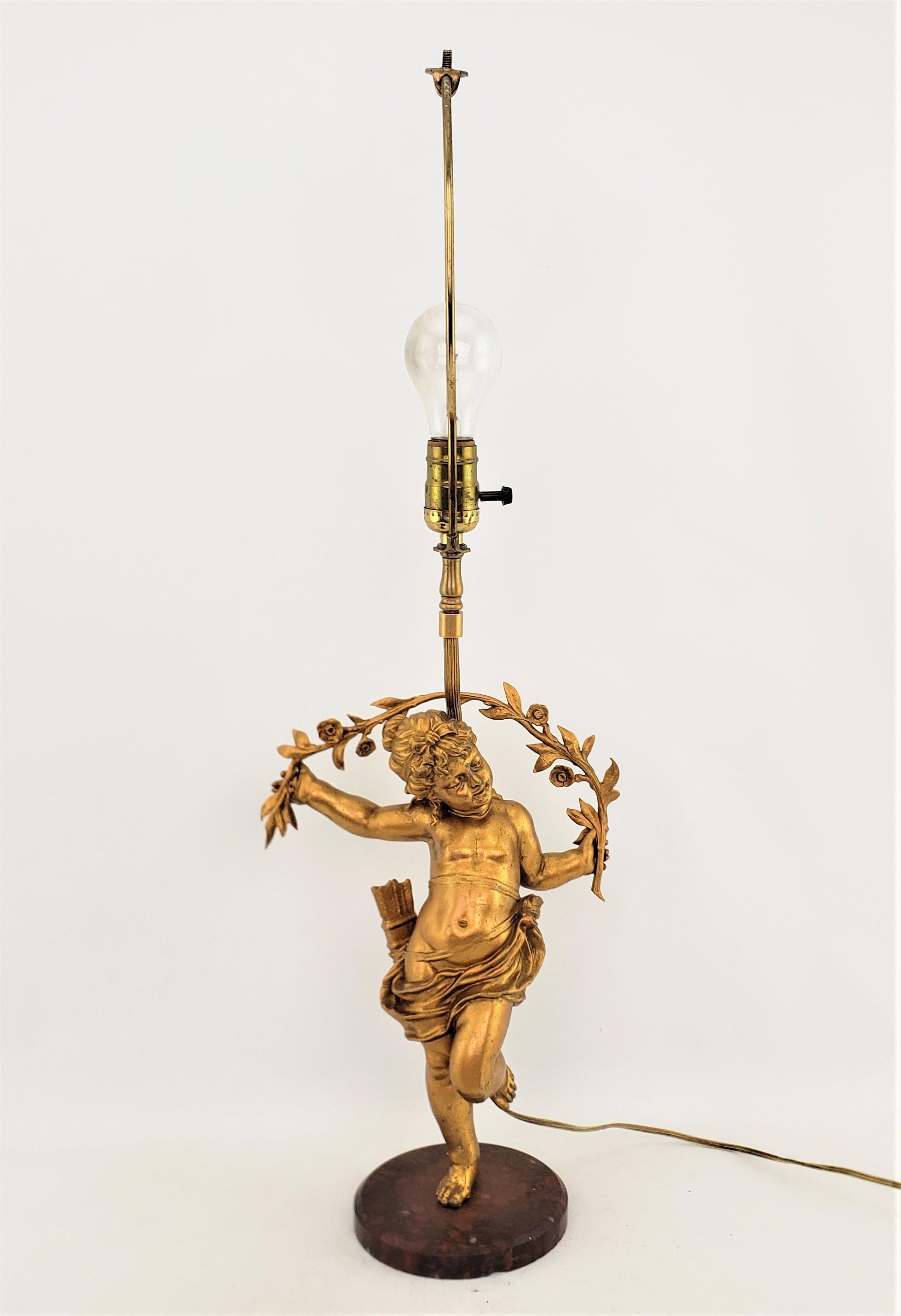 This antique table lamp is unsigned, but presumed to have originated from Italy and date to approximately 1920 and done in a Hollywood Regency style. The lamp features an ornately cast spelter cherub with a gilt finish and mounted to a red and black