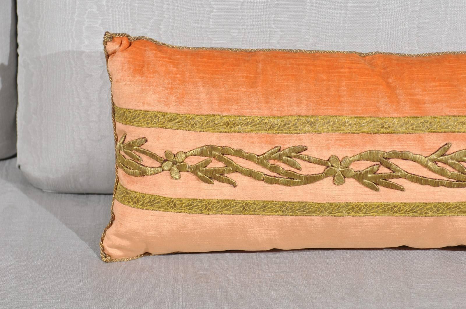 A long pillow made from an antique Ottoman Empire raised gold metallic embroidery on melon velvet. The pillow is adorned with a gold metallic vining embroidery and bordered with antique gold metallic galon. Hand trimmed with vintage fold metallic