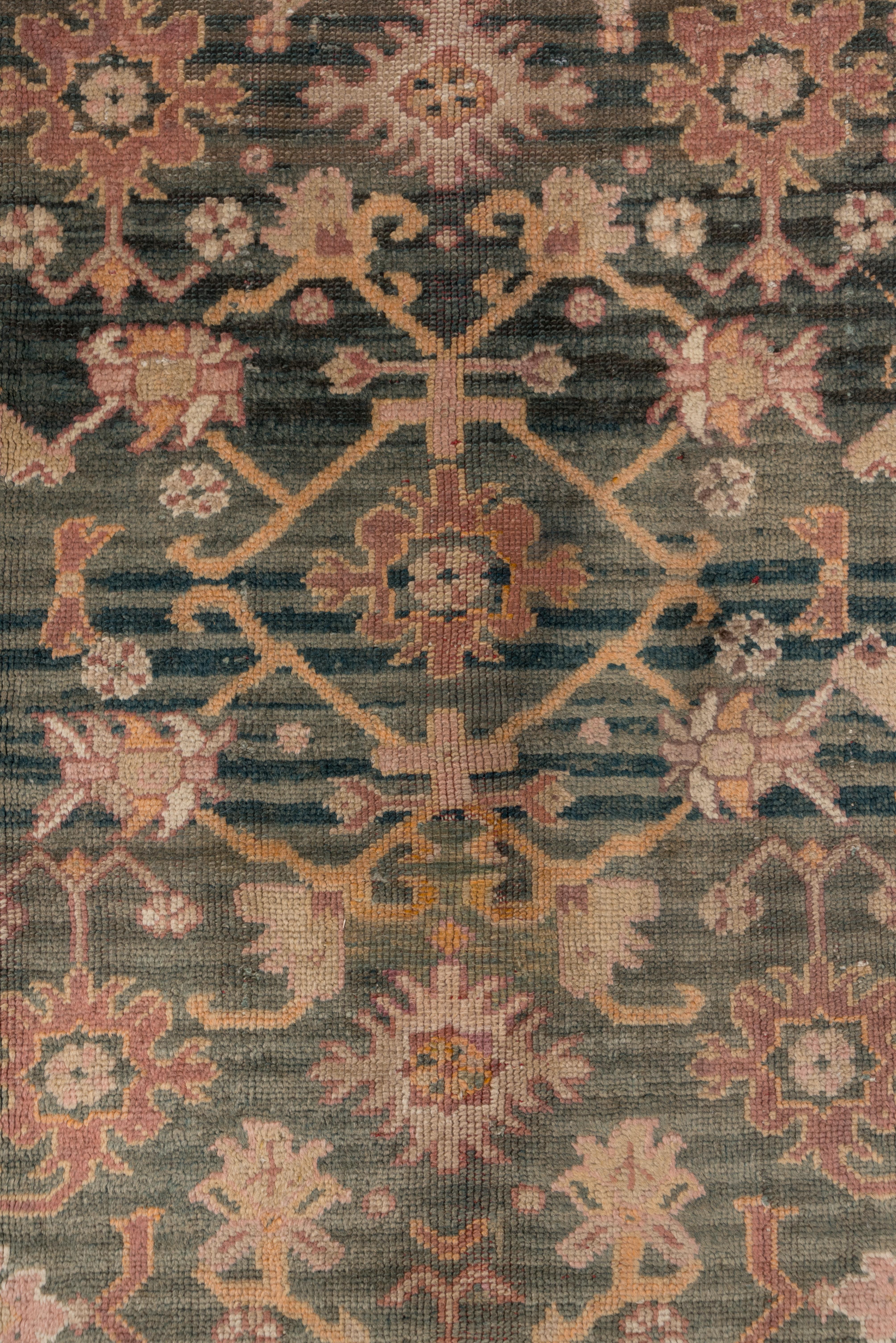 This softly colored western Anatolian carpet shows an abrashed soft rose-brown to striated aubergine-cherry ground with an all-over pattern of radiating stems and flowers, doubled leaves, open vinery lozenges and abstract jewelry forms. The narrow