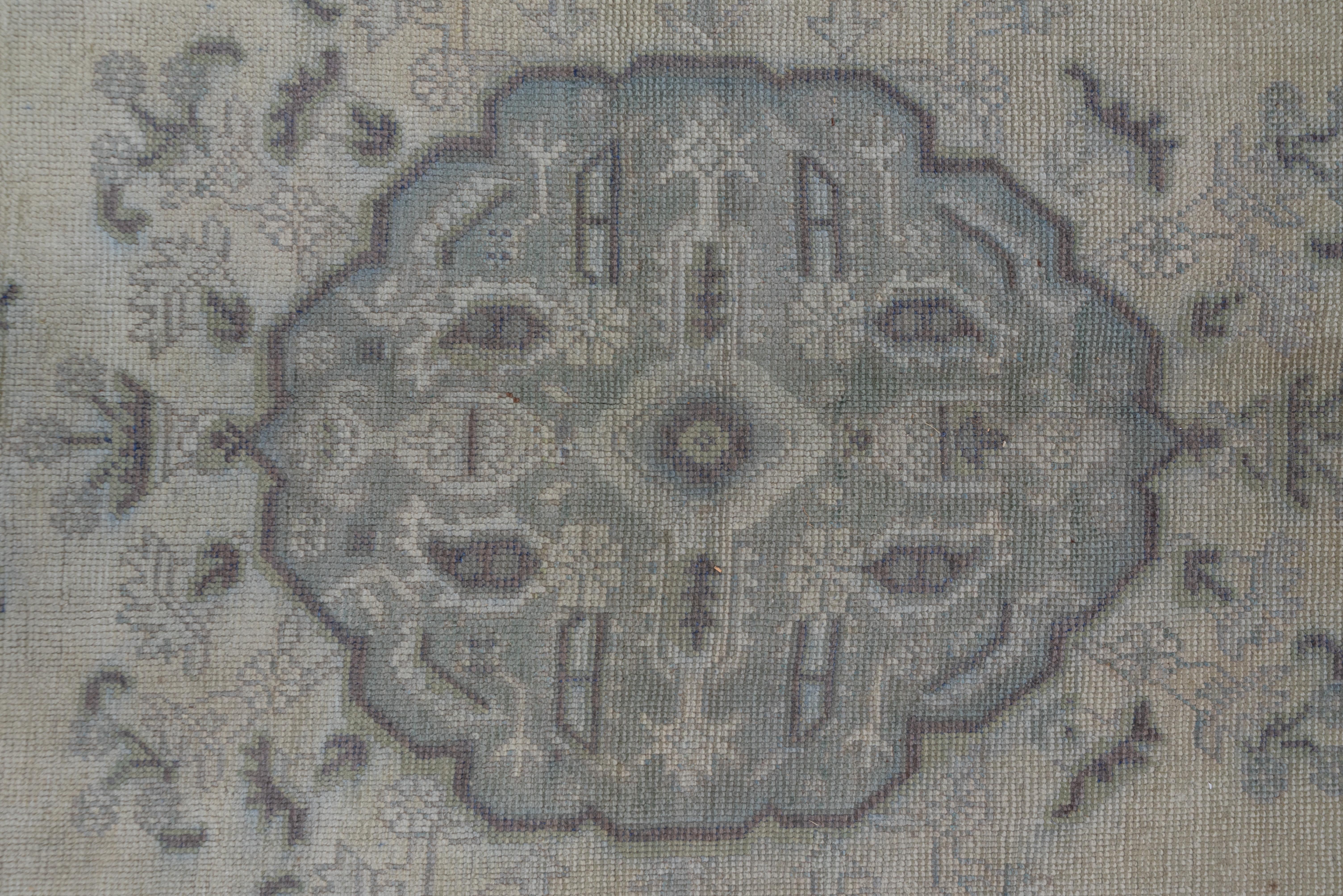 With a generally light tonality featuring sand and pale celadon with rust accents, this open field workshop carpet shows a lobed medallion within a leaf and flower wreath, and large escutcheon pendants. Both corners and border feature boteh-leaves.