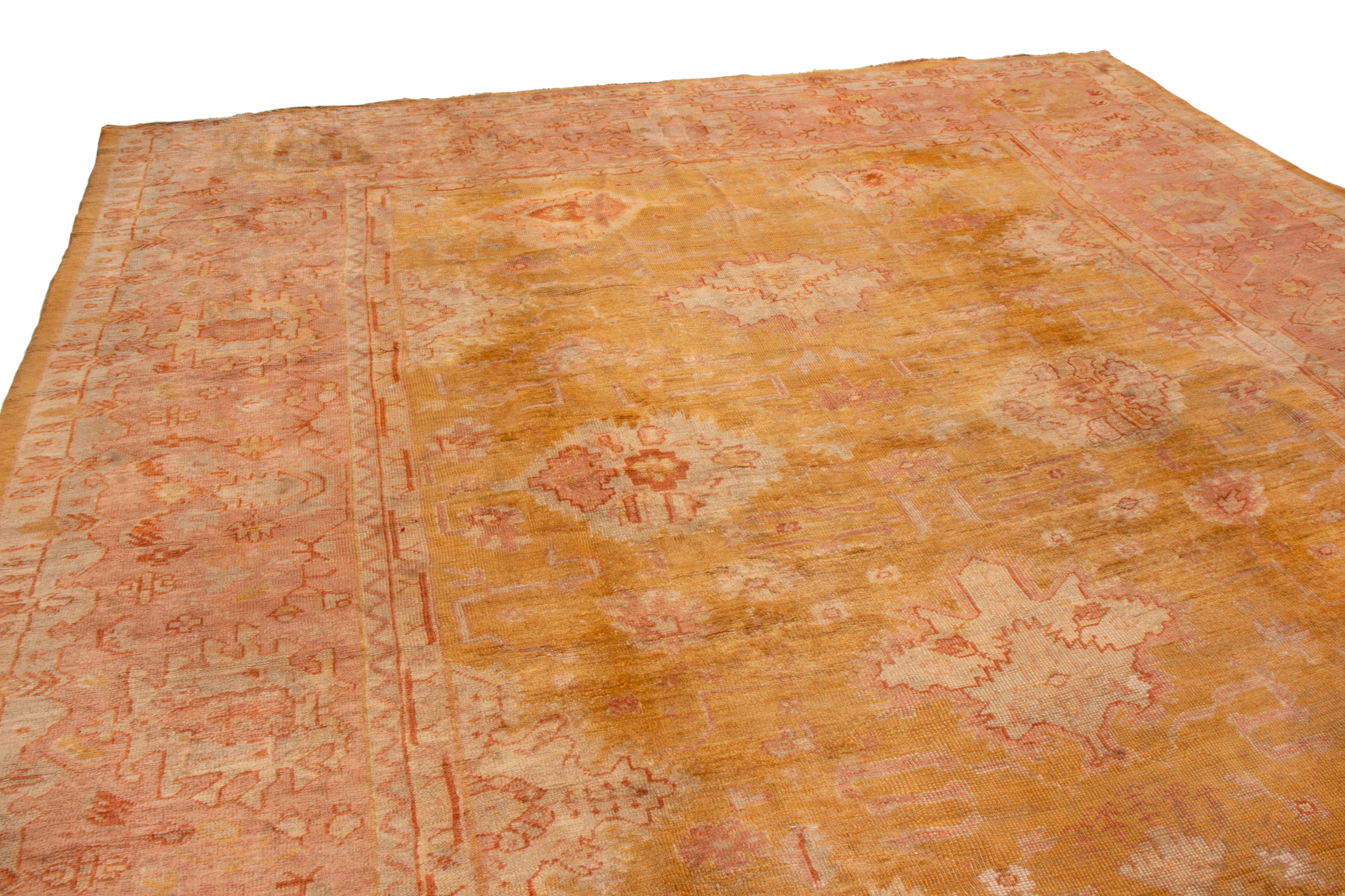 From 1900, this turn-of-the-century antique Oushak wool rug has geometric all-over patterns. The wide, highly stylized border is an atypically modern influence for a piece of the era, as is the combination of golden-orange, pinkish-red, and muted