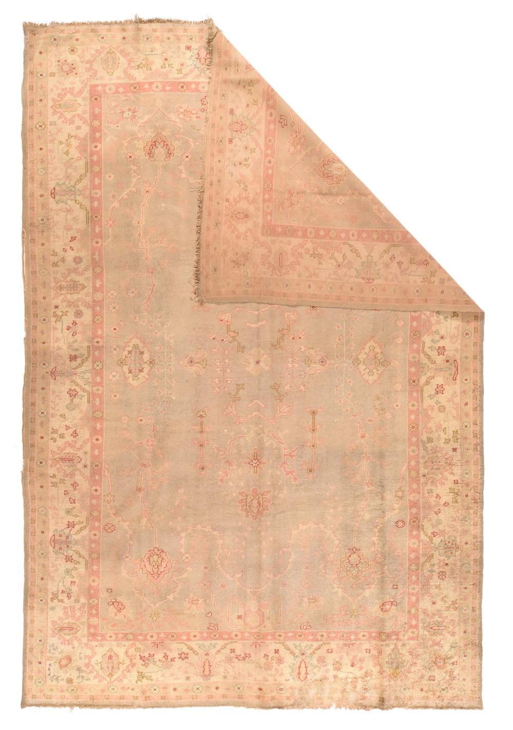 Tappeto antico Oushak 8'1'' x 11'10''. Un bordo color crema sabbioso con piante stilizzate a foglia lunga e delicati ramoscelli di fiori, incornicia il campo color mastice con cartigli galleggianti color sabbia, elementi vegetali e steli rigidamente