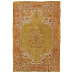 Tapis d'Oushak ancien à fond jaune et vert, bordure rose, accents rouges et orange