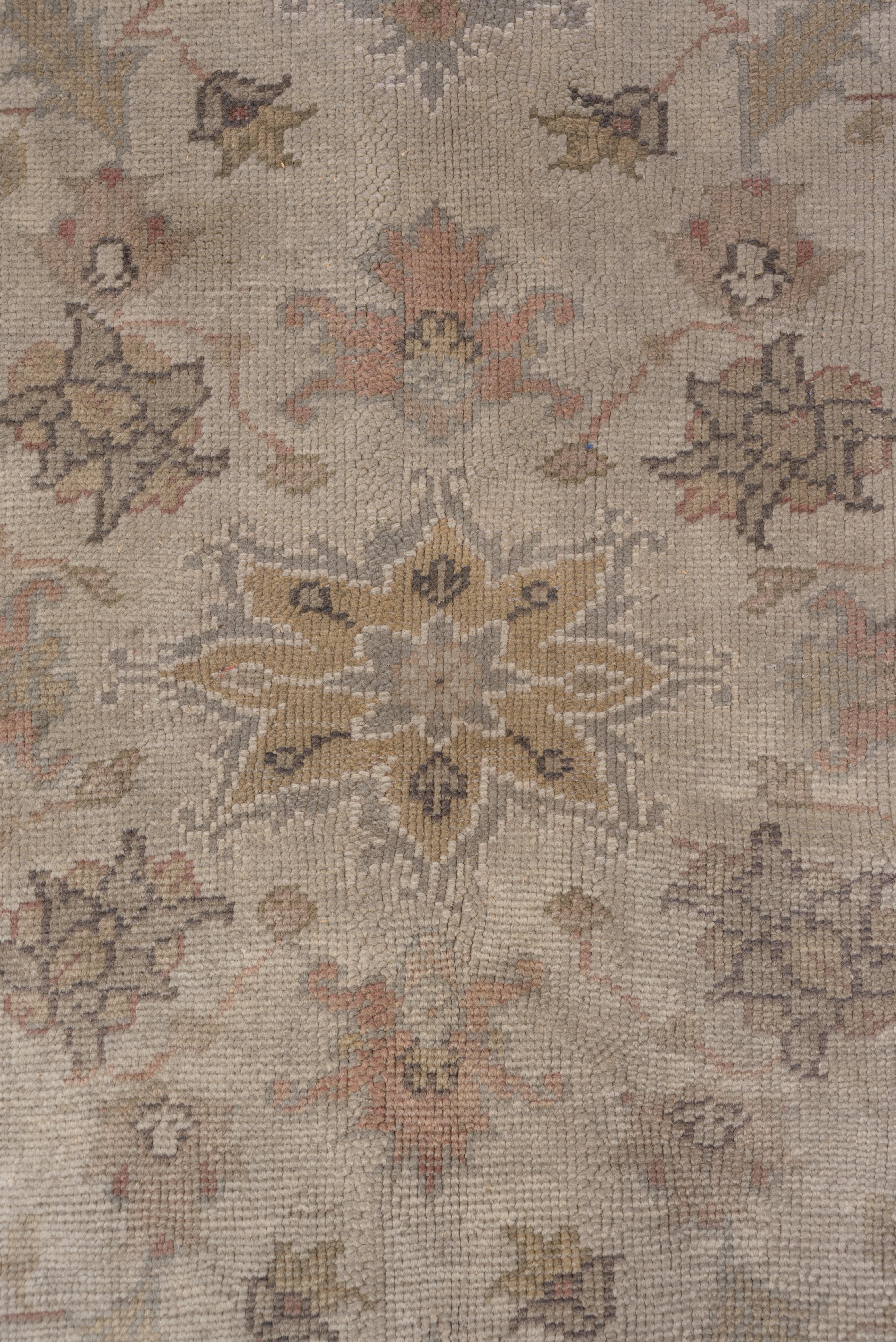 Palmette, steli spezzati, piccole foglie e fiori a rosetta formano un motivo all-over intorno a una palmetta/rosetta a petali più grande, dettagliata in tonalità buff, avorio e verde pallido su un campo beige sabbioso. Le palmette a foglia fluttuano
