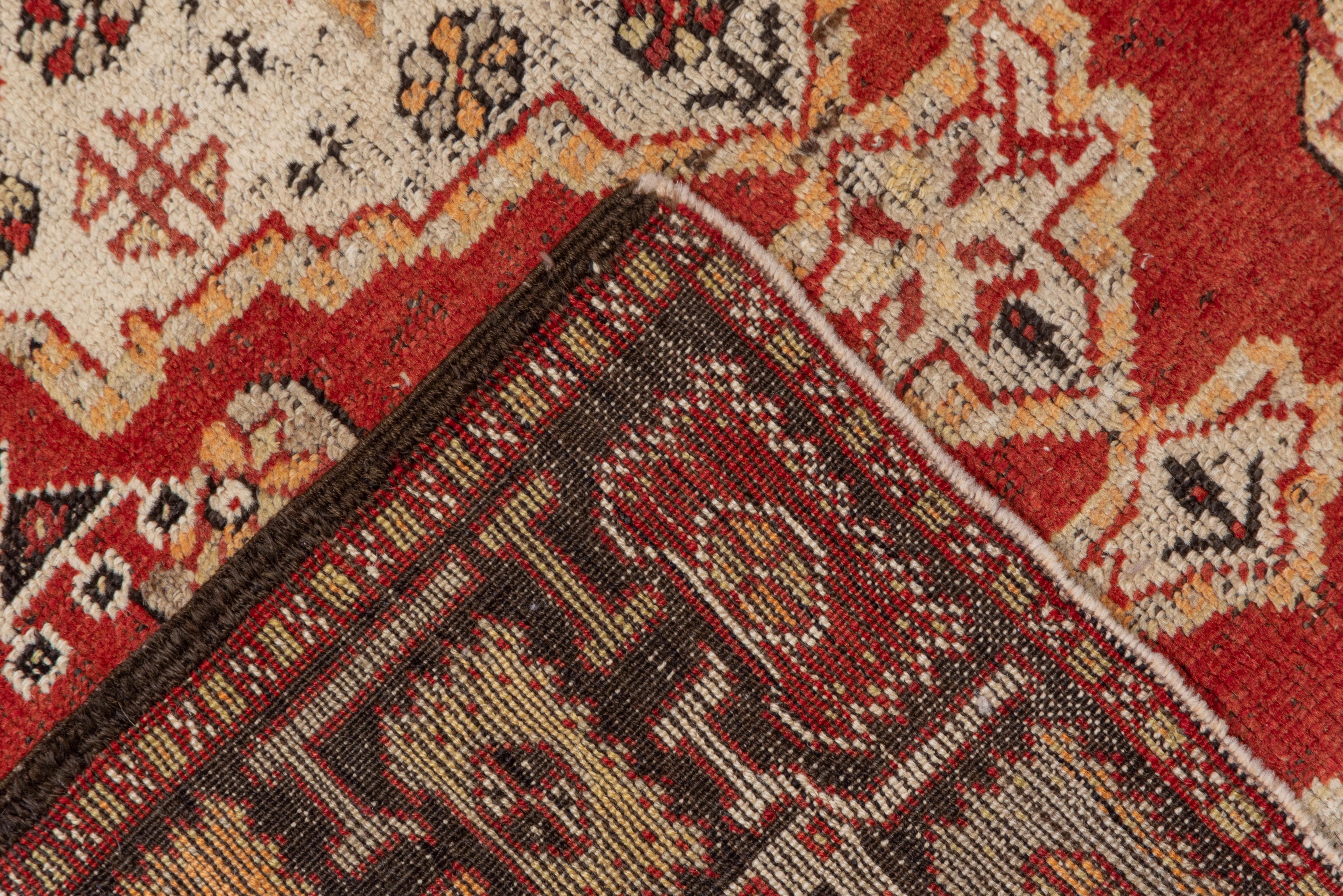 The red field features a doubly pendanted sand medallion within a scatter of stars and jewels. At each field, end is a panel displaying palmettes. The corroded brown border shows squared off stylized flowers with geometric stem fragments.
 