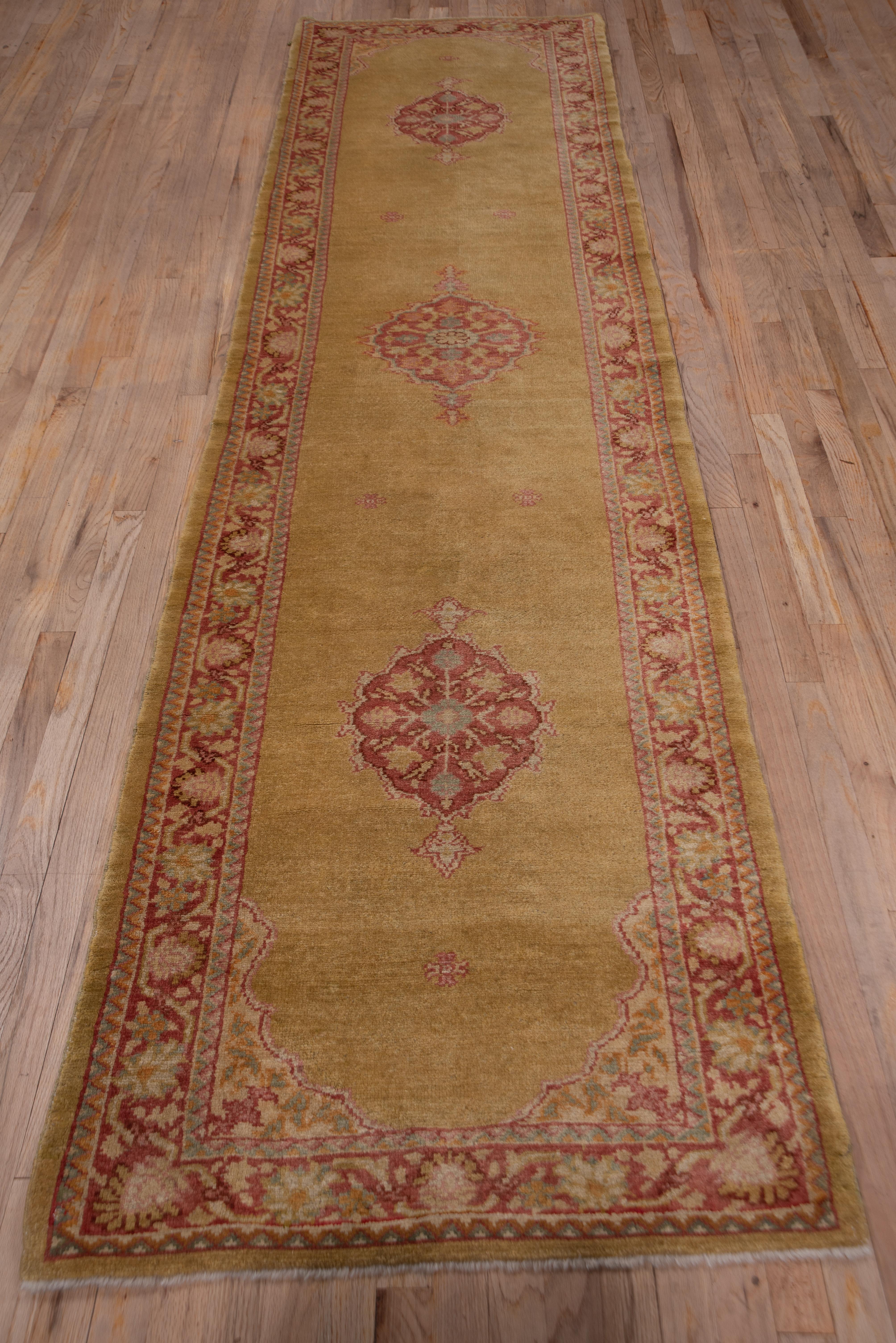 This solidly woven Turkish runner has a mustard gold field displaying three widely spaced small, scalloped, pendanted medallion. The red-brown min border features a palmette meander. The condition is generally very good, if not excellent., and the