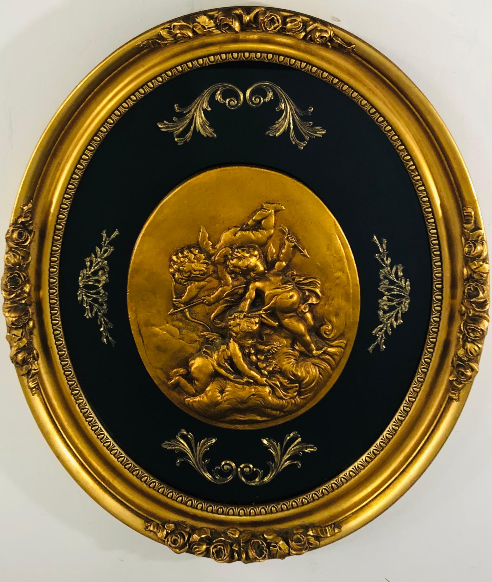 A classy and elegant hand painted oval plaque featuring winged cherubs holding arrows. The beautiful wall art is sculpted of wood and finely painted in gold. The cherubs are surrounded by black velvet background with bronze leaves design and a glass