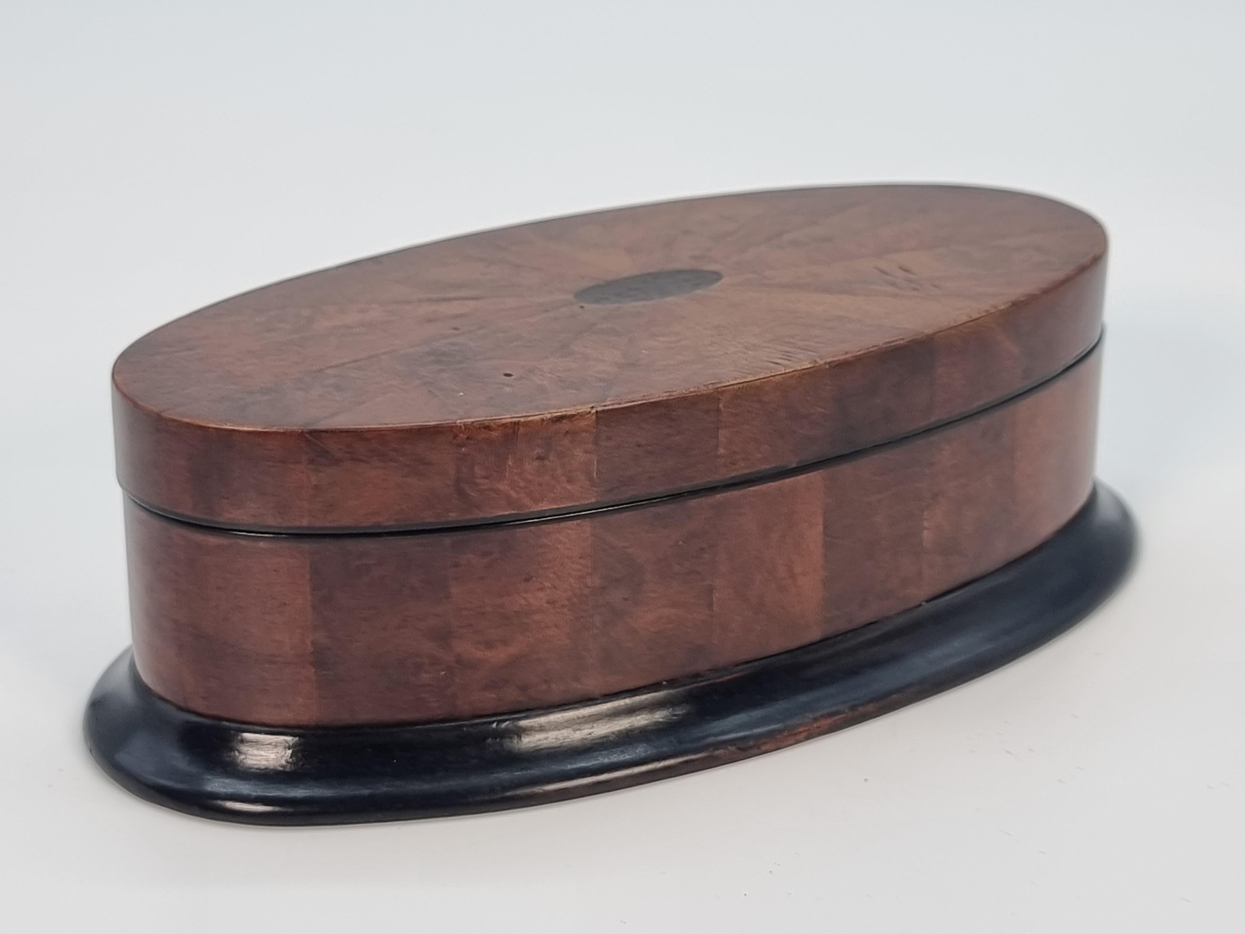 This beautiful small oval box is a very complicated piece of English cabinet making. It has been very precisely made with a perfectly fitted lid. The box sits on an ebonized moulded plinth. The sides are veneered in upright panels of various woods