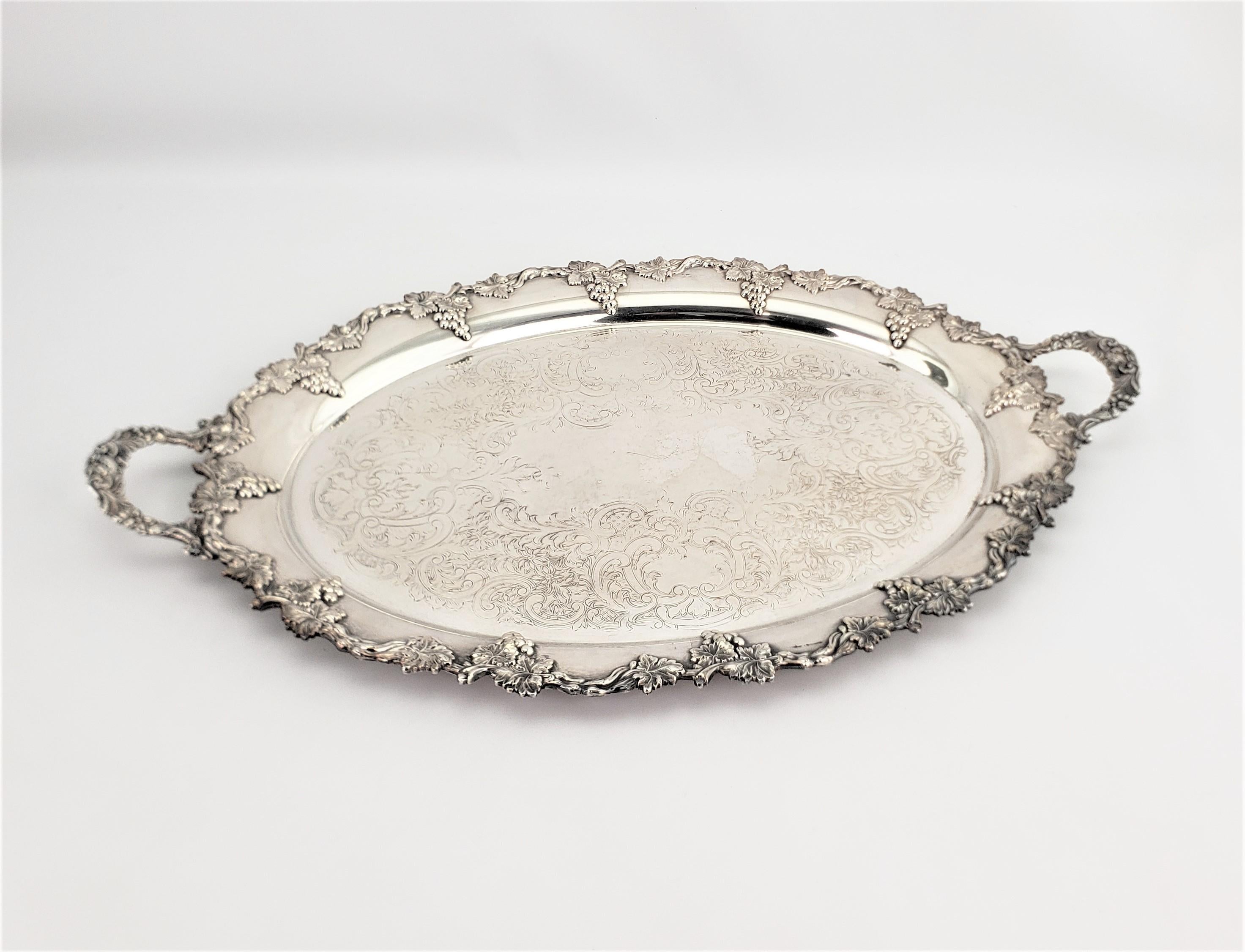 This oval silver plated serving tray was made in England by an unknown maker in approximately 1920 in a Victorian style. The tray is ornately decorated with a cast figural grape and leaf decoration on the surround and replicated on the handles. The