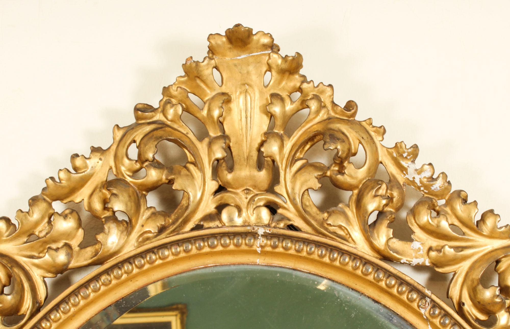 This is a fabulous large 4ft antique Italian Florentine giltwood mirror, Circa 1880 in date.

The oval mirror consists of a superbly carved cresting to the top and bottom, the frieze is decorated with  hand carved floral and foliate motifs with