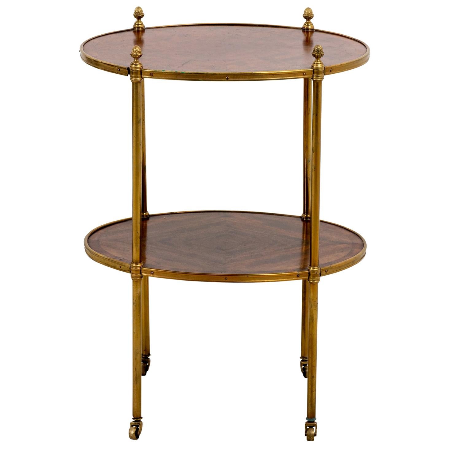 Antique oval fruitwood two tiered side table with brass banding, brass casters, and brass acorn shaped finials, circa 1930s. Made in England. Please note of wear consistent with age including patina and oxidation to the metal.