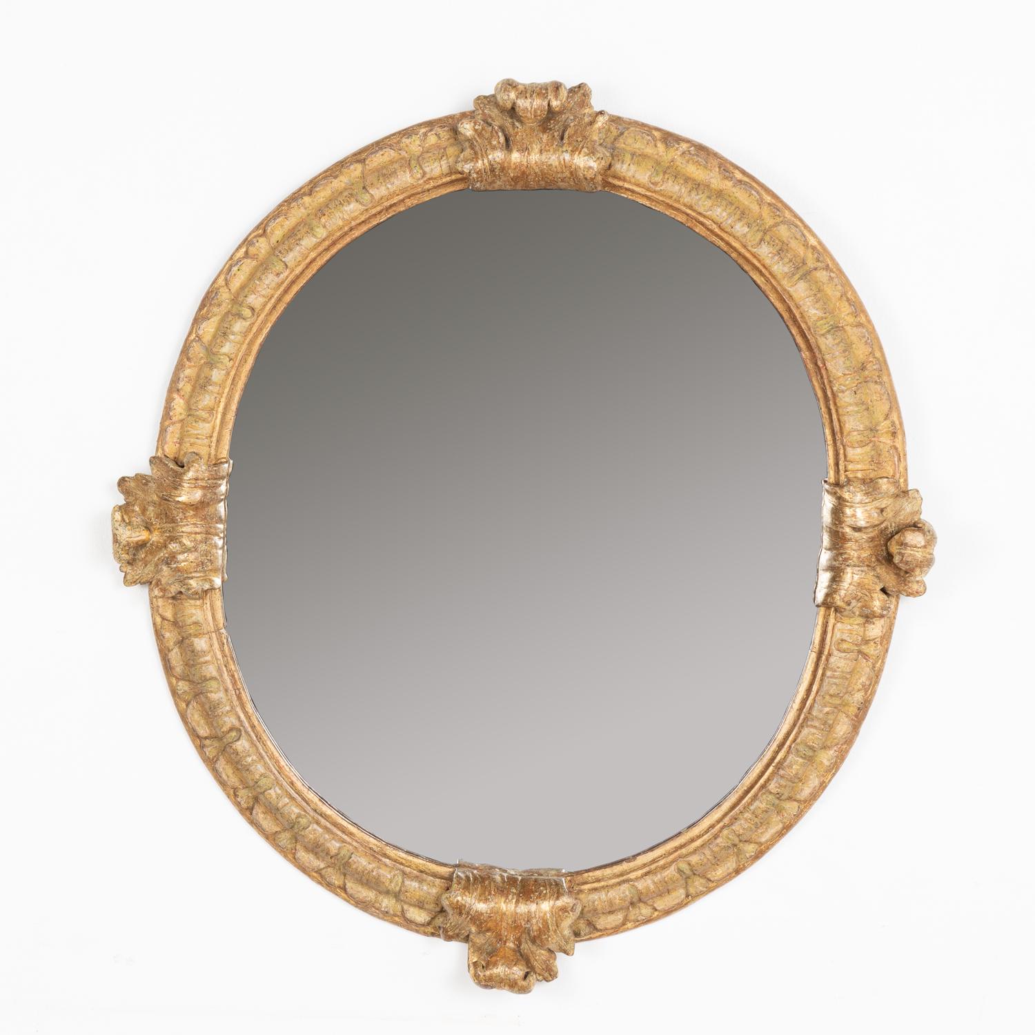 This impressive gold gilt mirror has four dramatic carved flourishes accenting the slightly oval frame.
There is expected age-related wear as seen where the gilt has been worn off, wood is nicked or cracked but wear does not impact the beauty nor