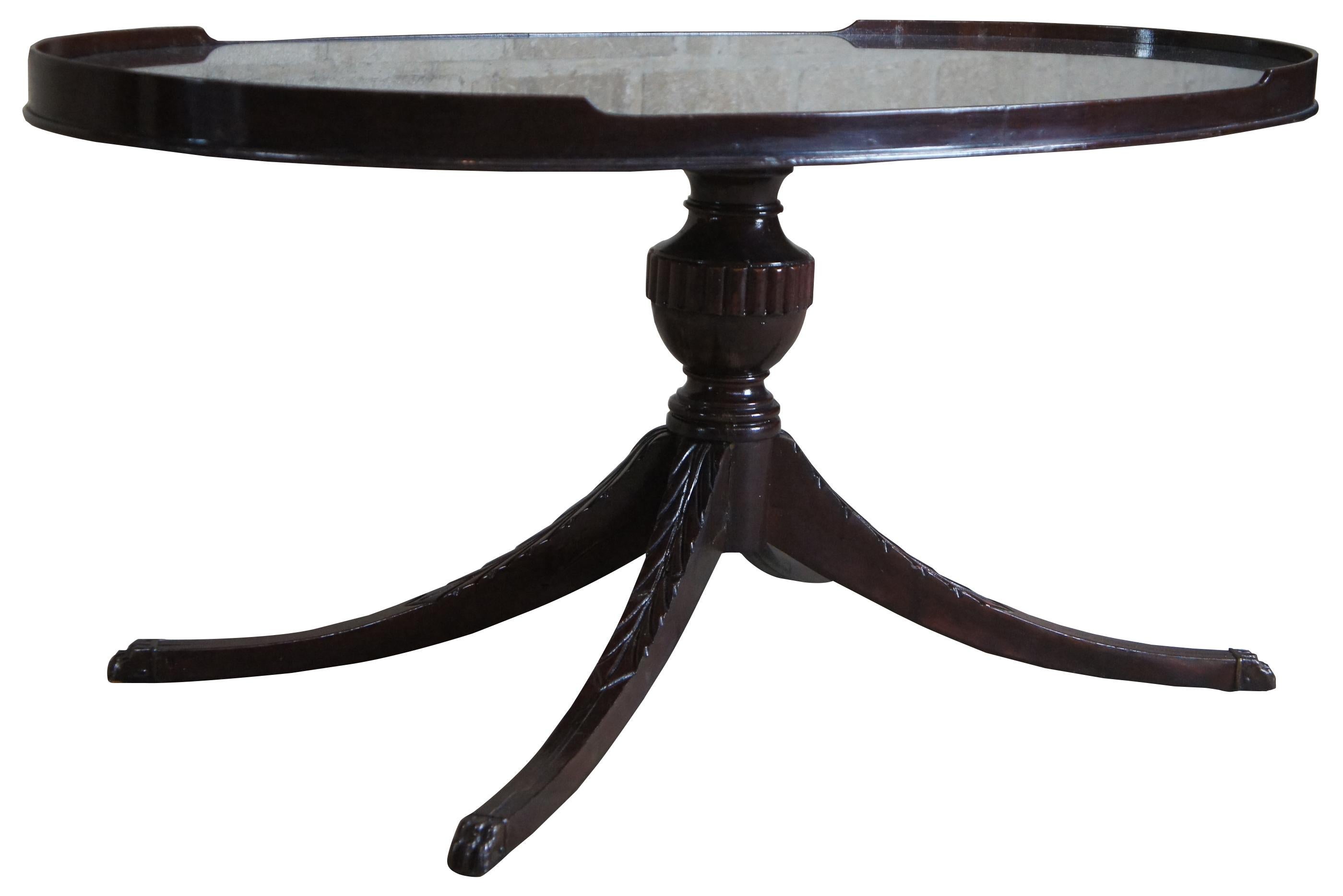 Circa 1940s Duncan Phyfe coffee or tea table. Made from mahogany with an oval form. Features a glass inset top supported by a turned baluster leading to four legs capped with brass paw feet. Measures: 36