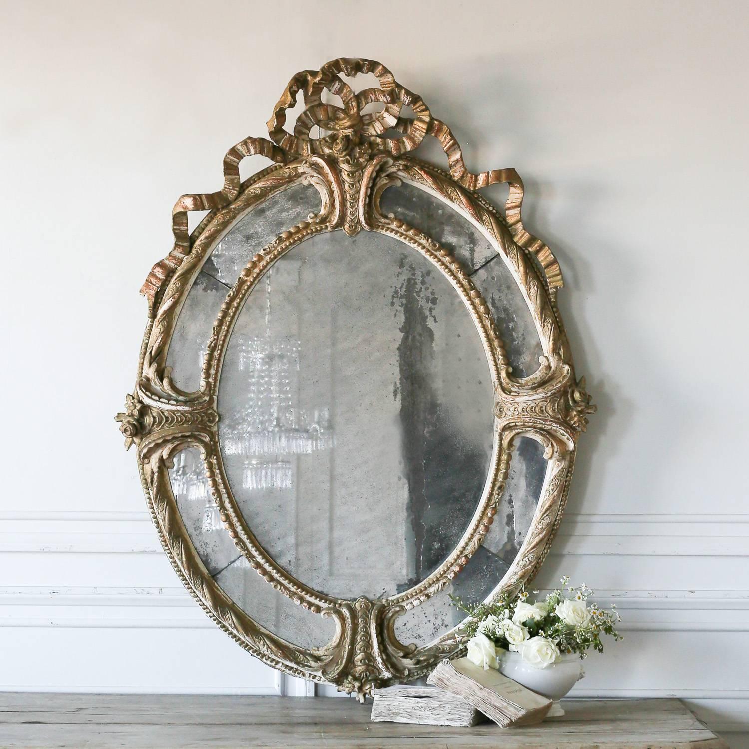 Antique oval mirror with heavily distressed, original mercury glass. A large bow crest sits atop this multi-sectioned mirror with large fern-like waves adorning the sides. Four divided sections create a unique design inspiring a special connection