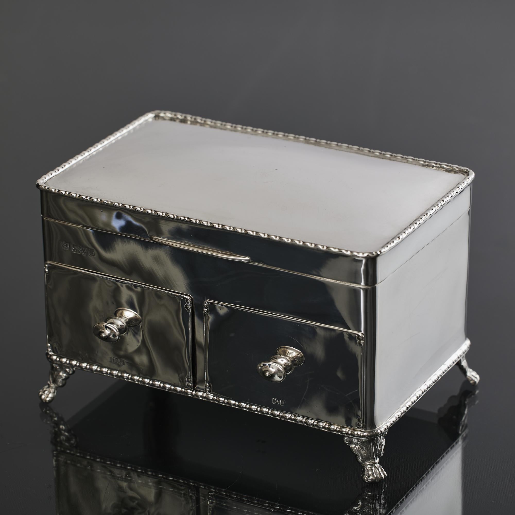 Boîte à bijoux en argent ancien, fabriquée à la main à la fin de l'époque édouardienne, montée sur quatre supports à griffes et à feuilles, comportant deux tiroirs en bois à façade argentée et un couvercle à charnière bordé de dorures.
 
 Le plateau