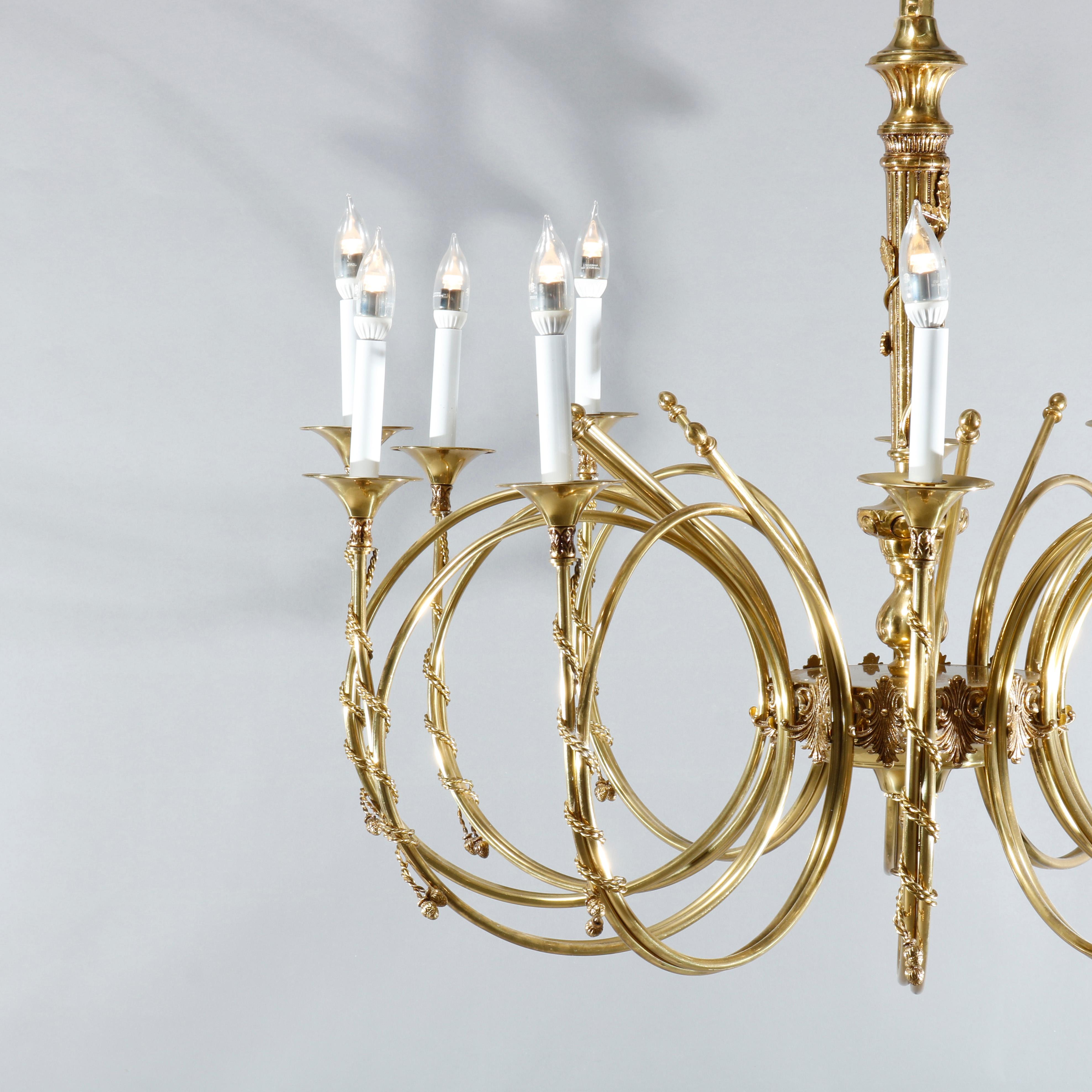 A large and antique French Empire chandelier offers brass frame with central reeded column having foliate vine wrap and twelve French Horn or Trumpet form scrolled arms wrapped in tassels and terminating in candle lights, 20th century

Measures: 47